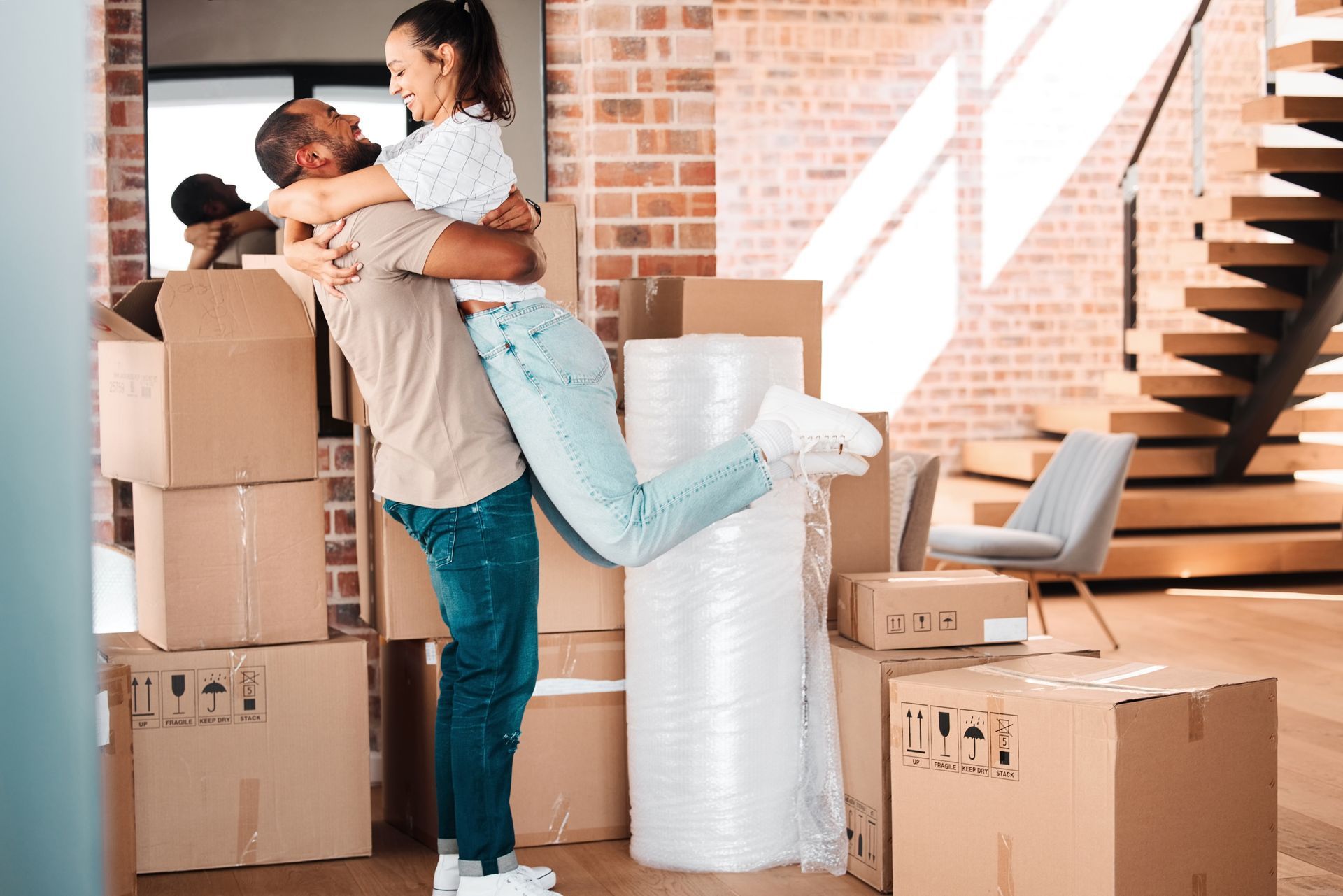 Man lifting woman in a hug, surrounded by moving boxes in a new home.