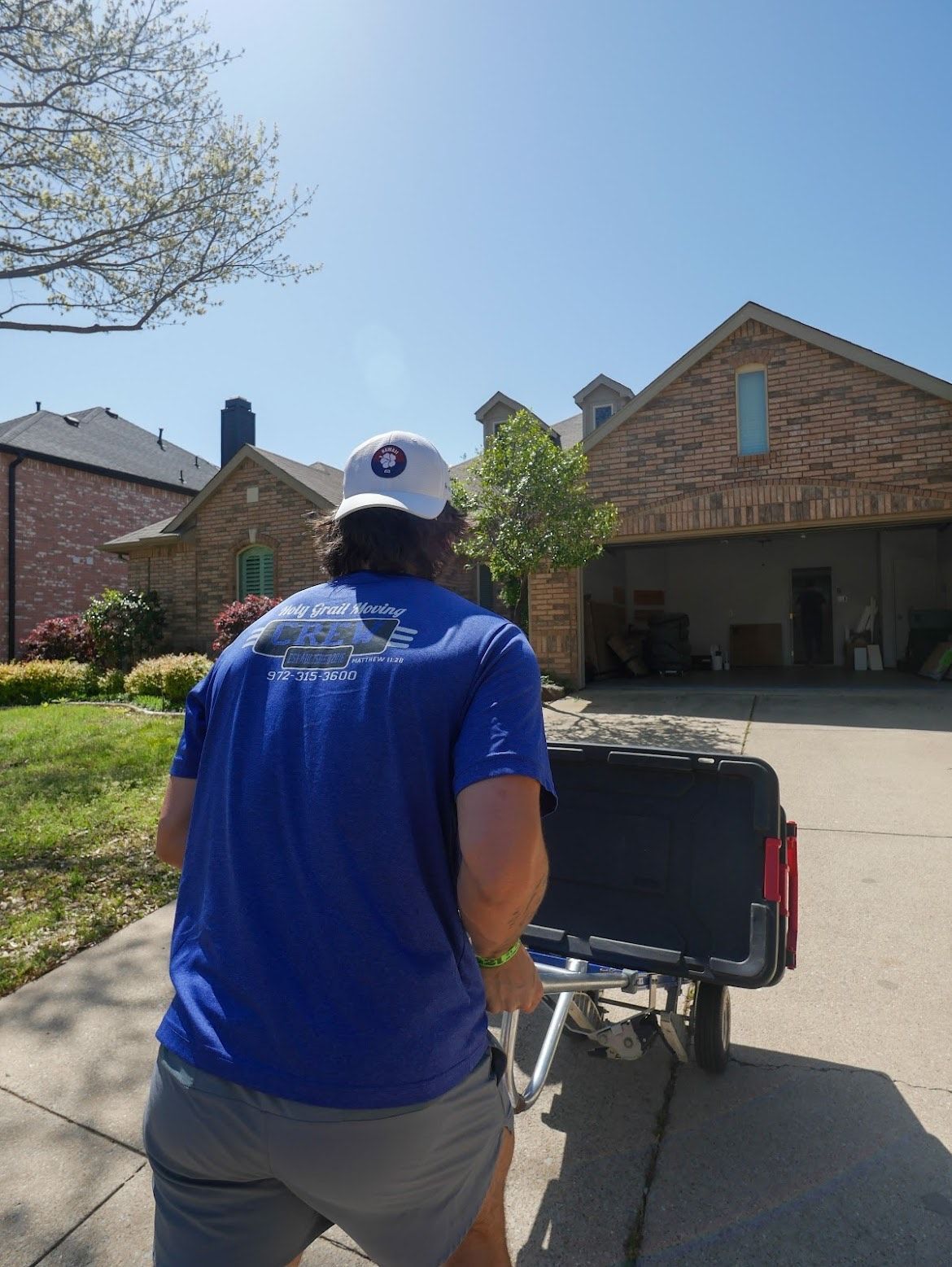 A man in a blue shirt is pushing a cart in front of a house