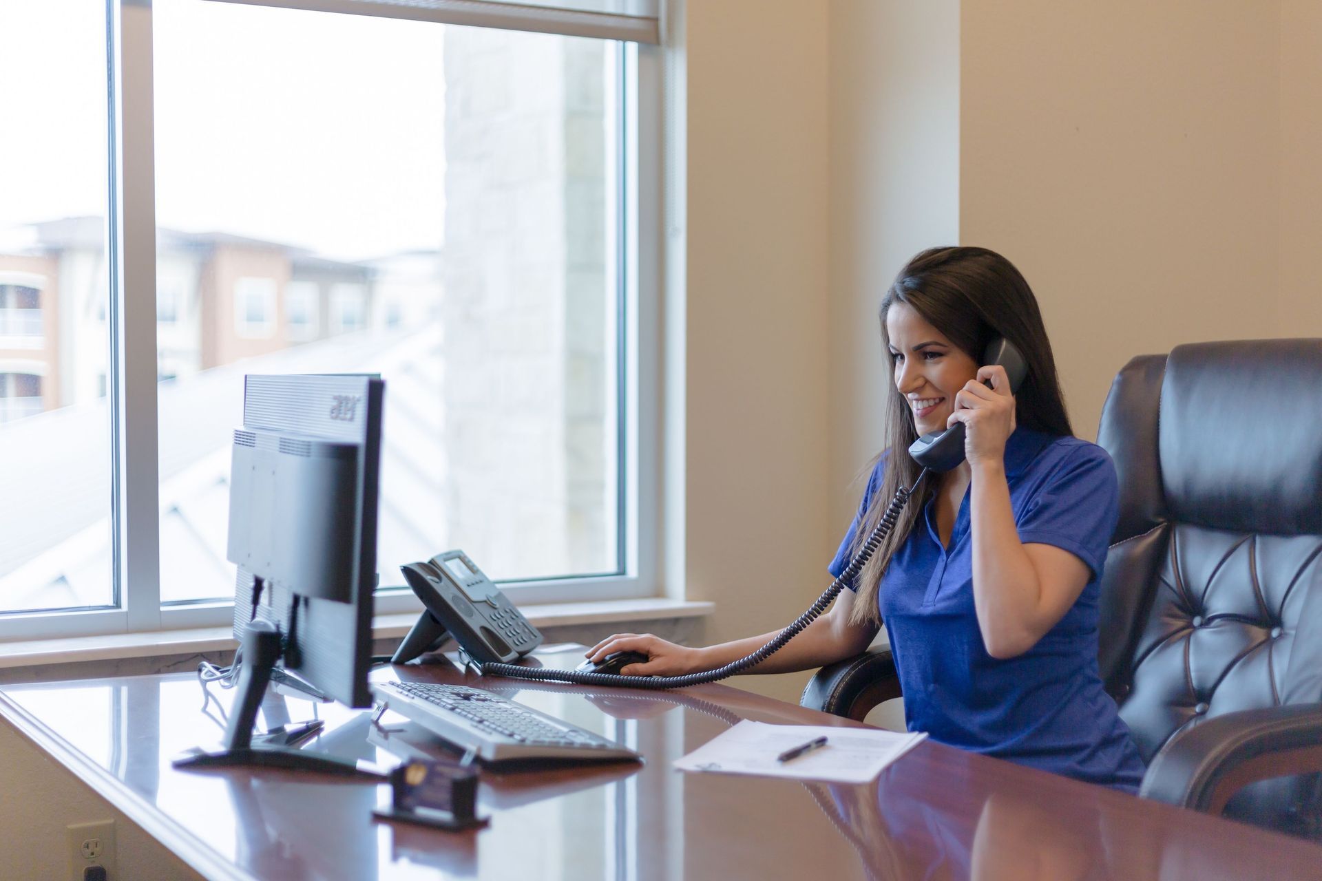 A woman is sitting at a desk talking on a phone.