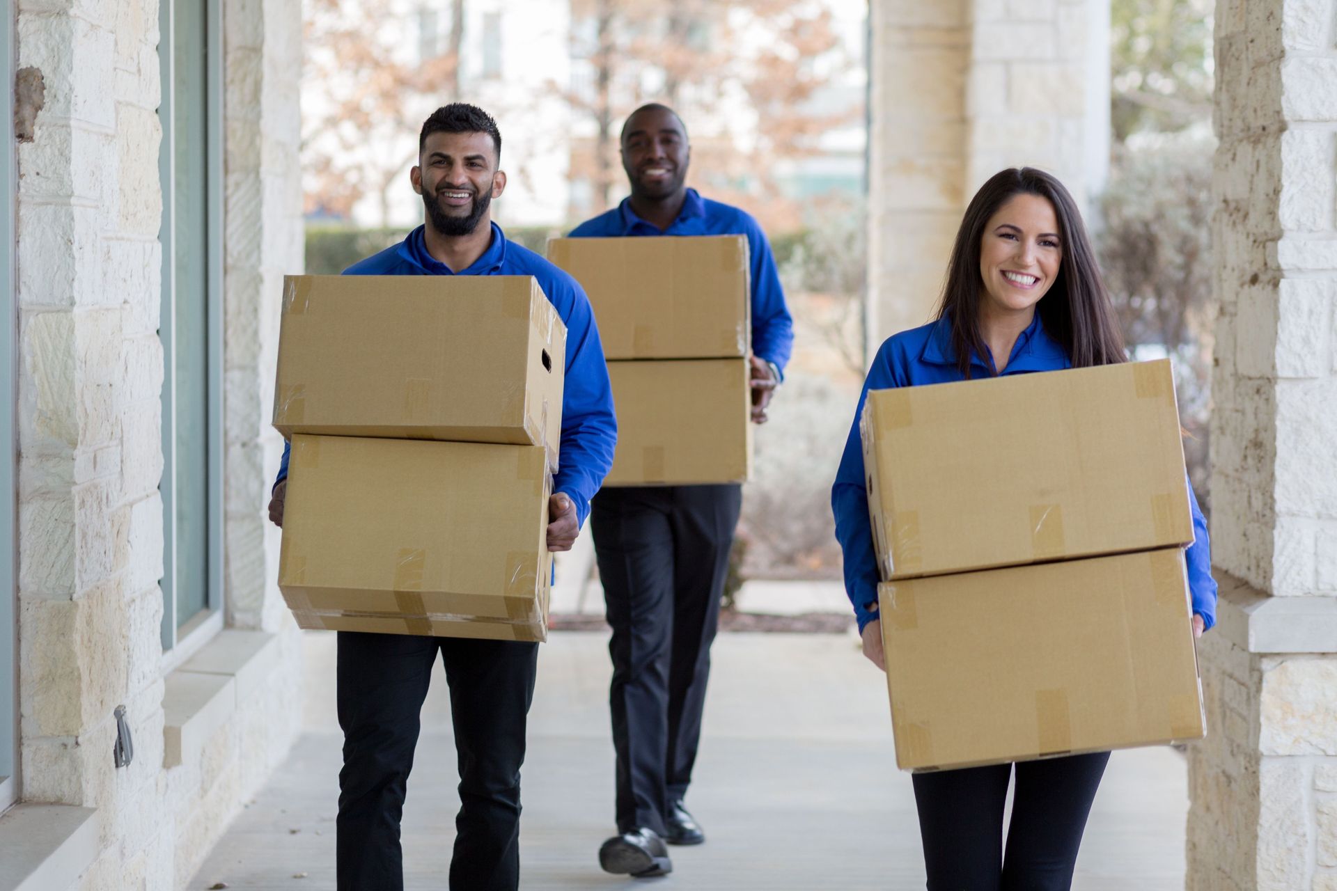 A group of movers are carrying boxes down a sidewalk.