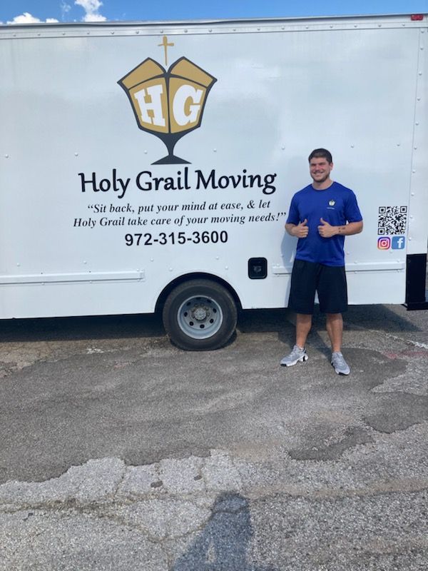 A man is standing in front of a holy grail moving truck.