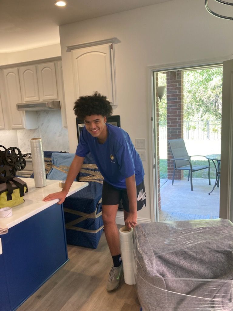 A young man is standing in a kitchen holding a roll of plastic wrap.