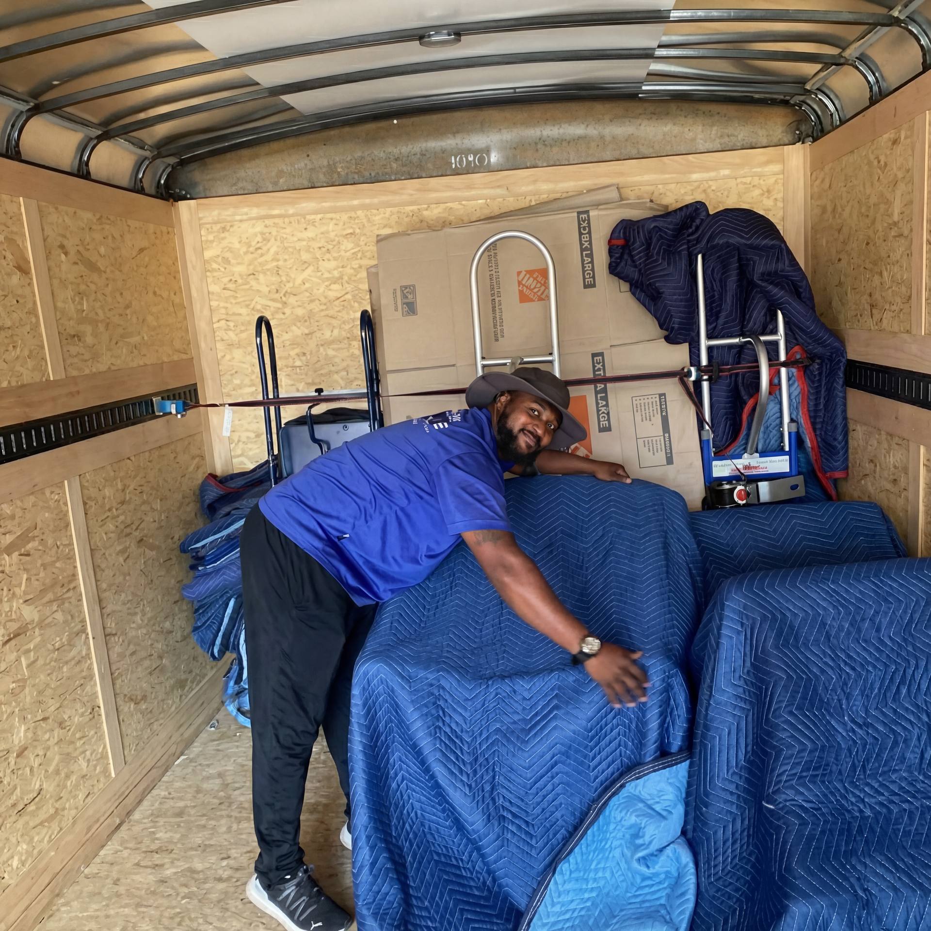 A person in a blue shirt hugs a wrapped blue chair inside a moving truck filled with boxes and equipment.
