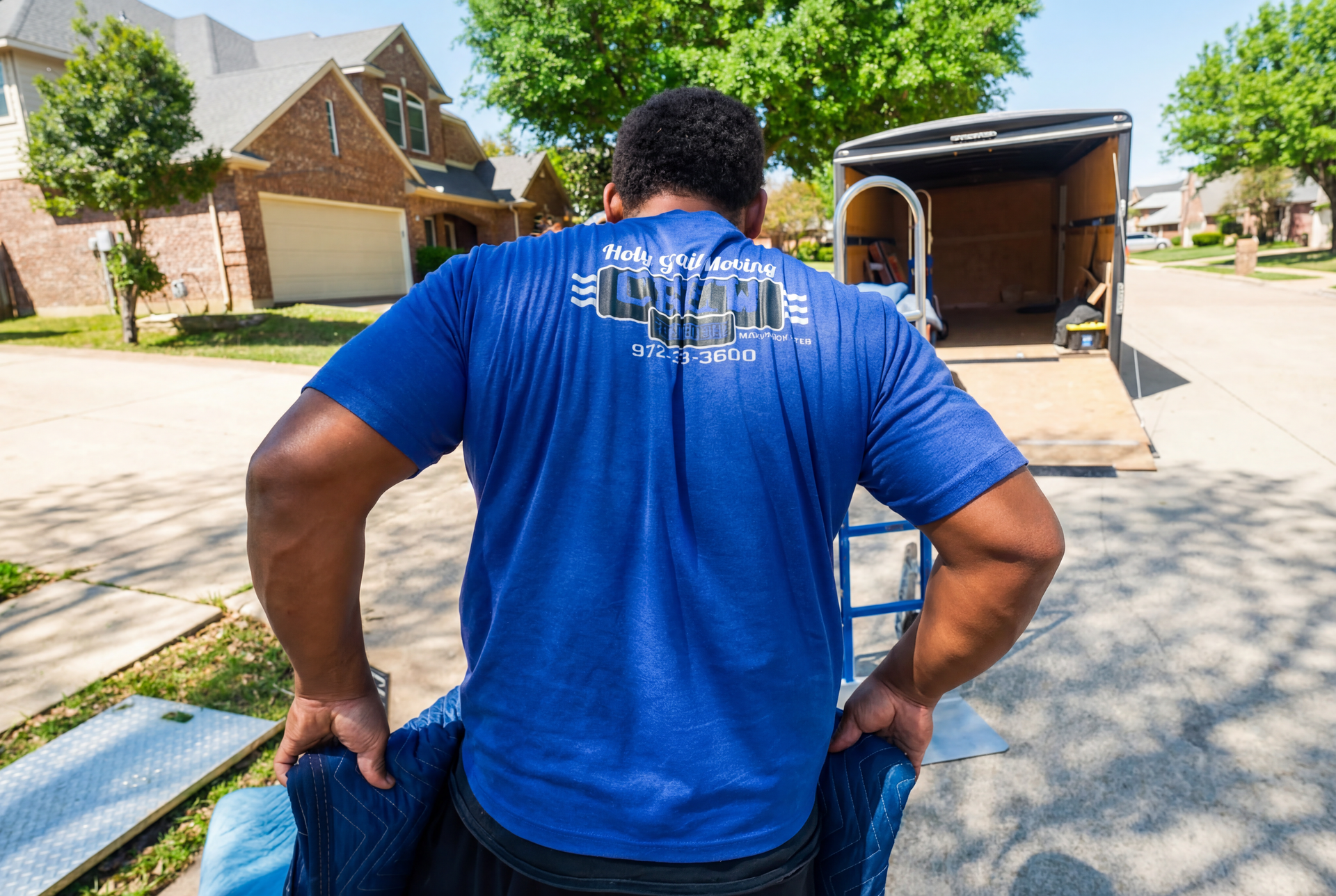 A person in a blue shirt loads a moving truck with furniture on a sunny day.