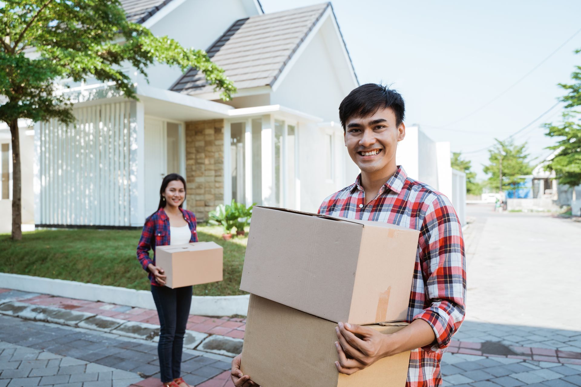 A man and a woman are holding cardboard boxes in front of a house.