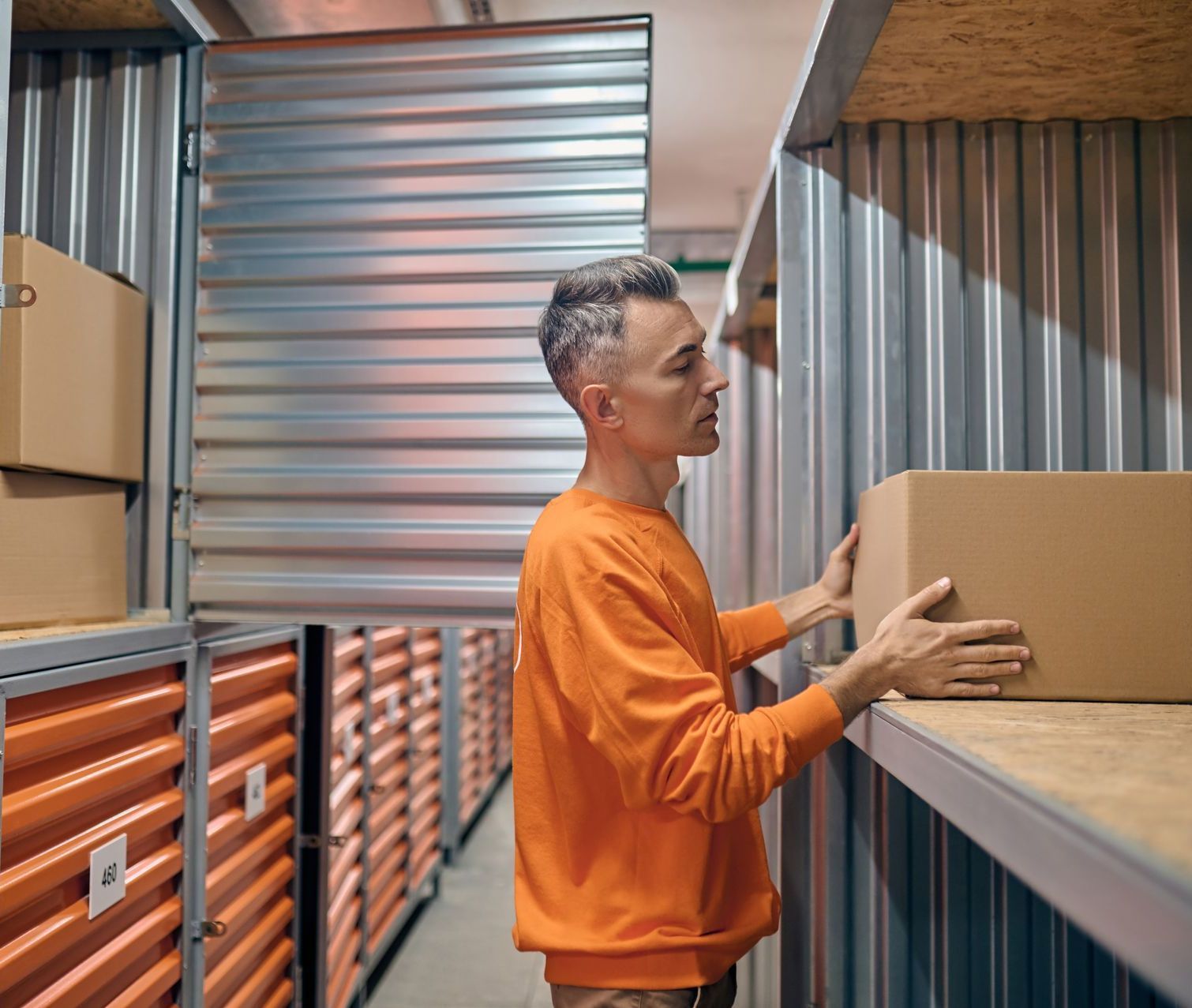 A man is holding a cardboard box in a storage room.