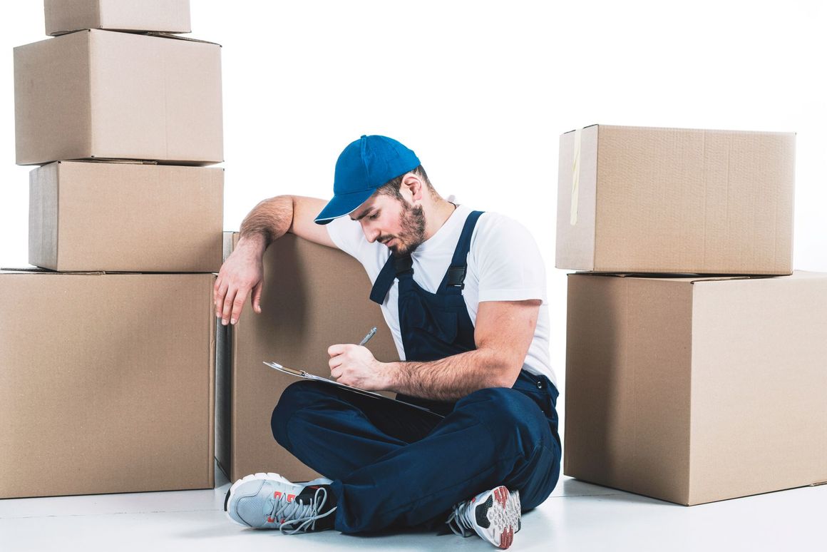 A man is sitting on the floor next to a pile of cardboard boxes.