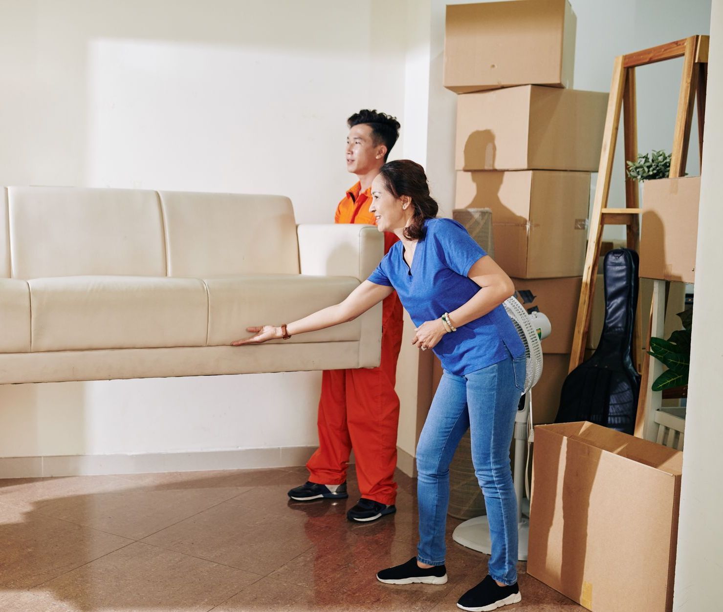 A man and a woman are carrying a couch in a living room.