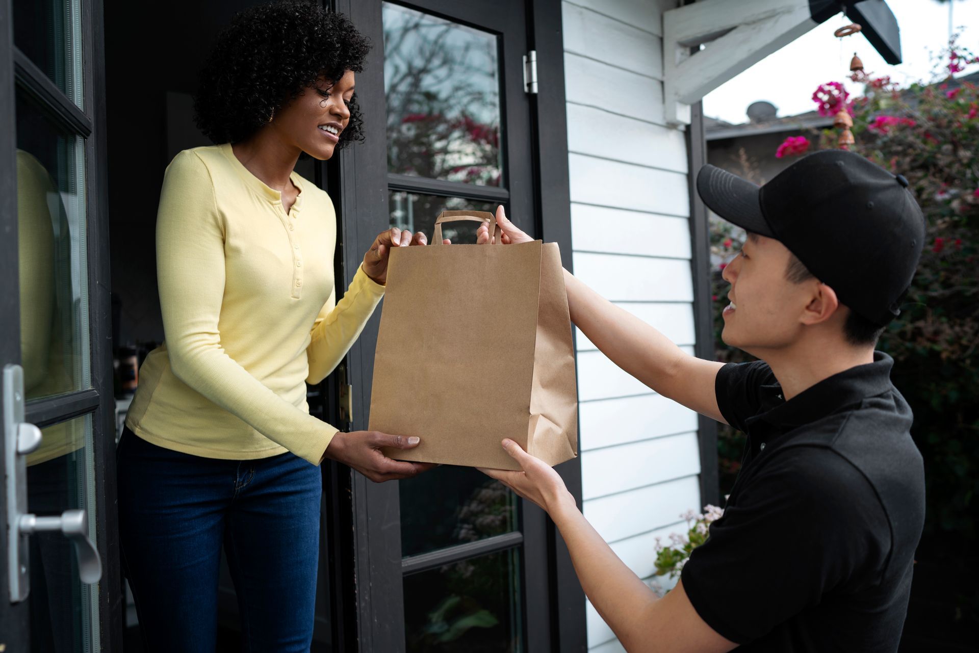 A man is delivering a bag of food to a woman in a doorway.