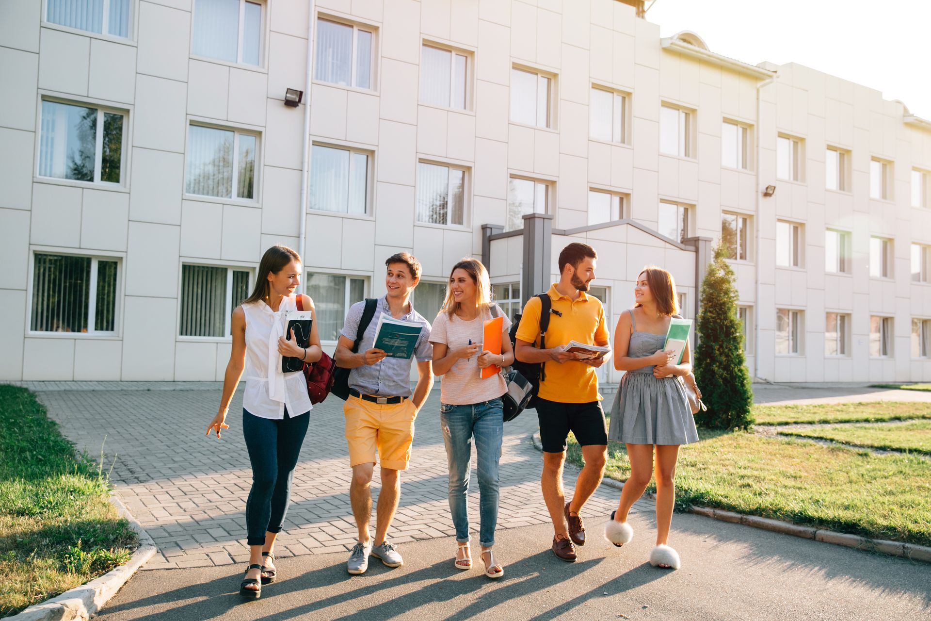 A group of young people are walking down a sidewalk in front of a building.