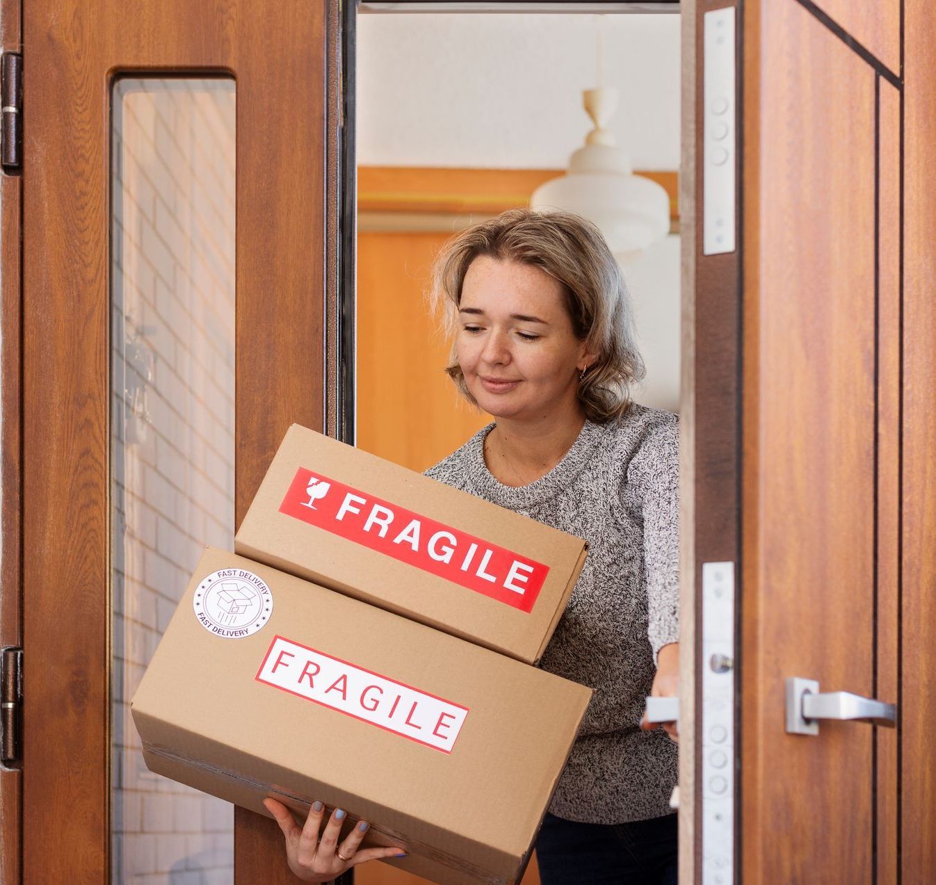 A woman is holding two fragile boxes in front of a door.