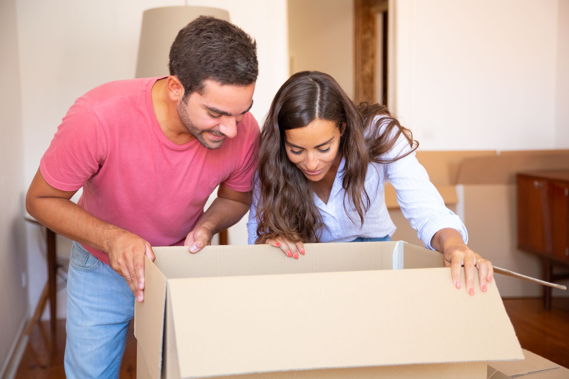 A man and a woman are opening a cardboard box in a living room.