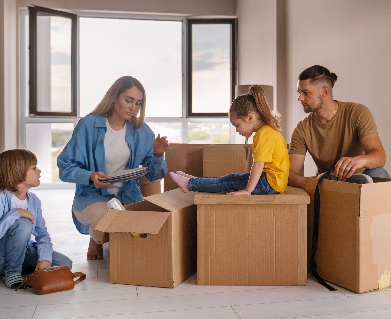 A family is sitting on cardboard boxes in a new home.