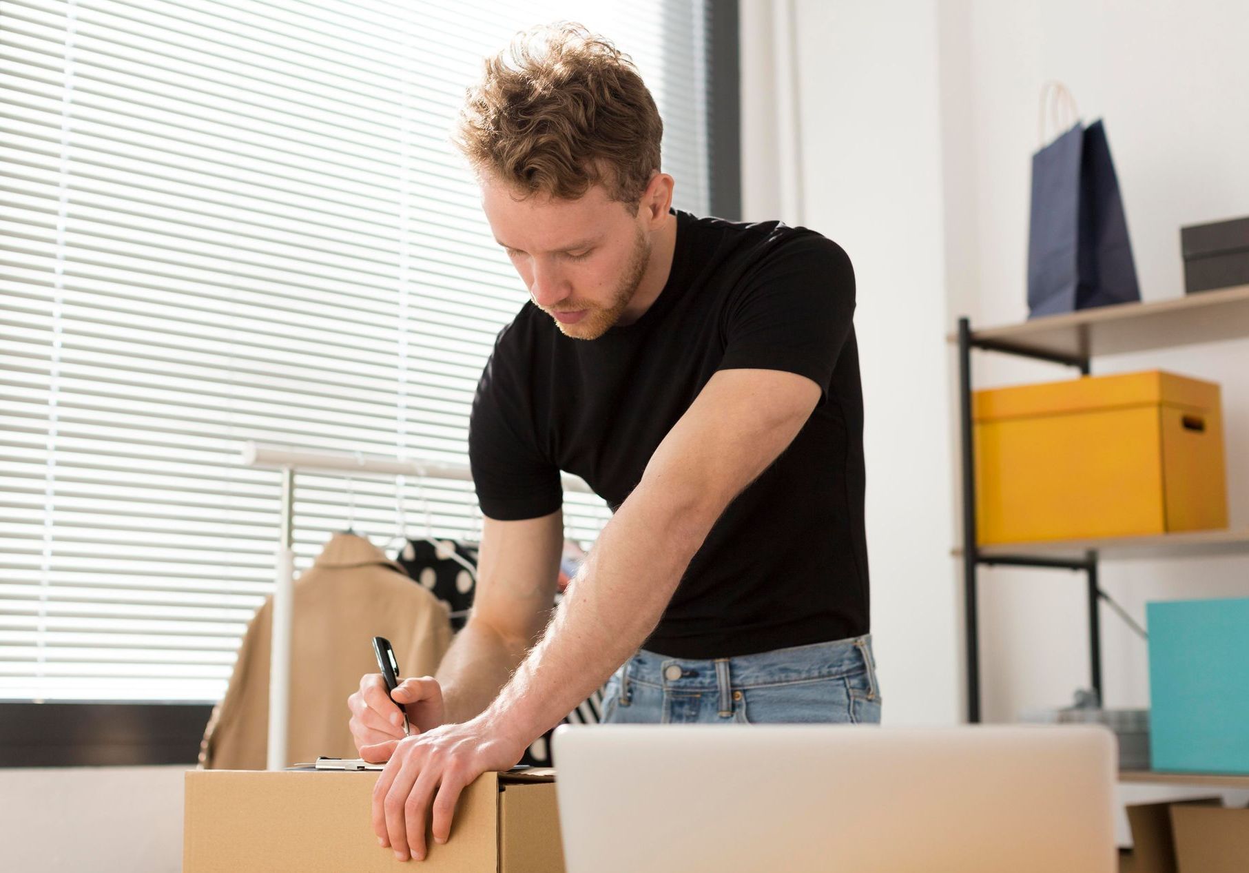 A man is writing on a piece of paper while standing next to a cardboard box.