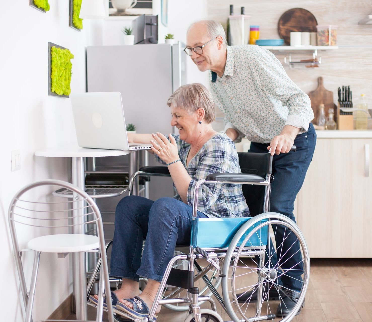 A man is helping an elderly woman in a wheelchair use a laptop computer.