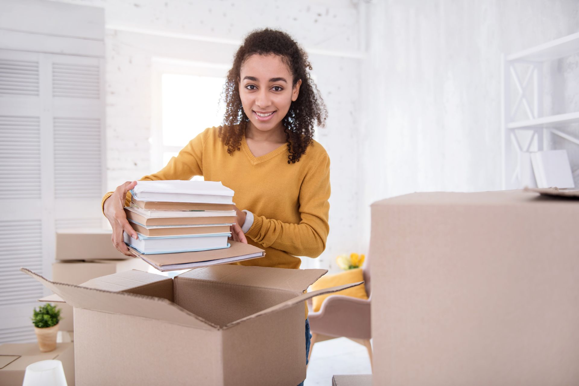 A woman is holding a stack of books in a cardboard box.