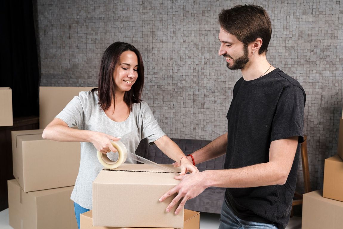 A man and a woman are packing boxes in a living room.