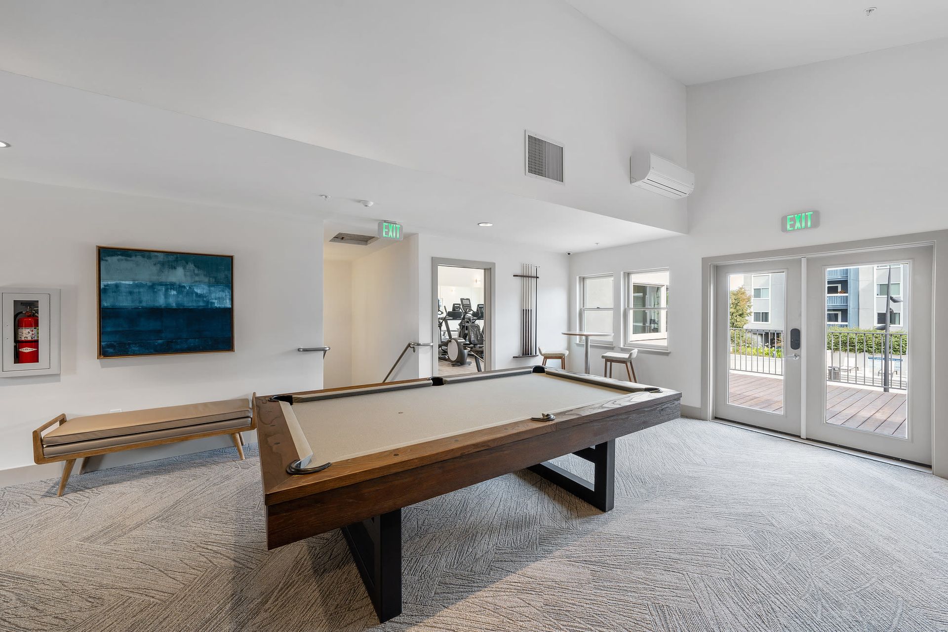 Indoor community recreation room with a billiards table, bench seating, and exit doors.