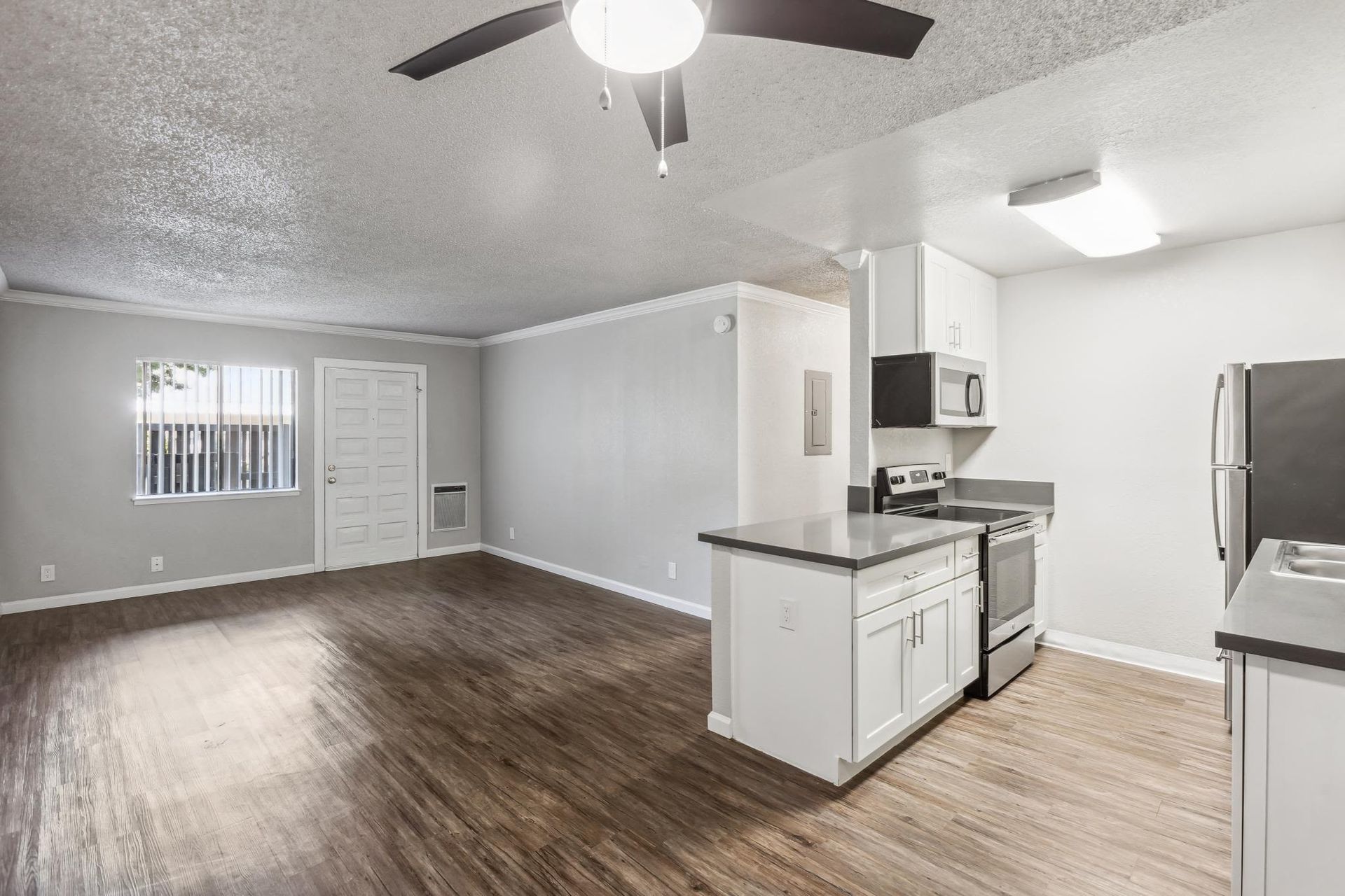 Open-concept living area with a kitchen, white cabinets, stainless steel appliances, wood-look flooring, and a ceiling fan.