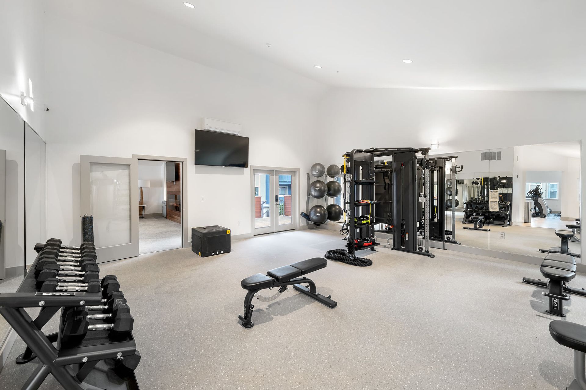 Bright on-site community gym with free weights, benches, and a large mirrored wall.