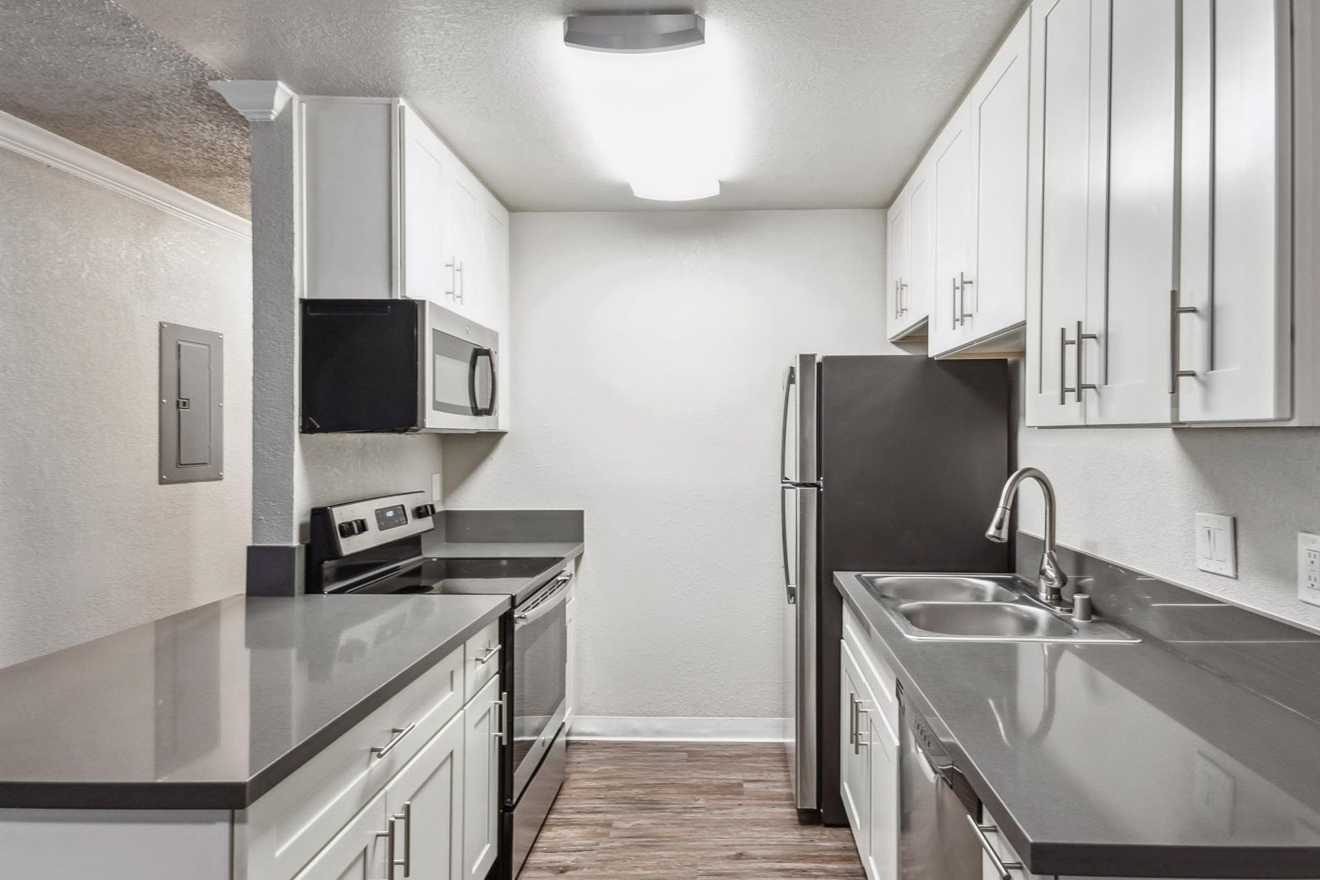 Compact apartment kitchen with white cabinets, stainless steel appliances, and a double sink.