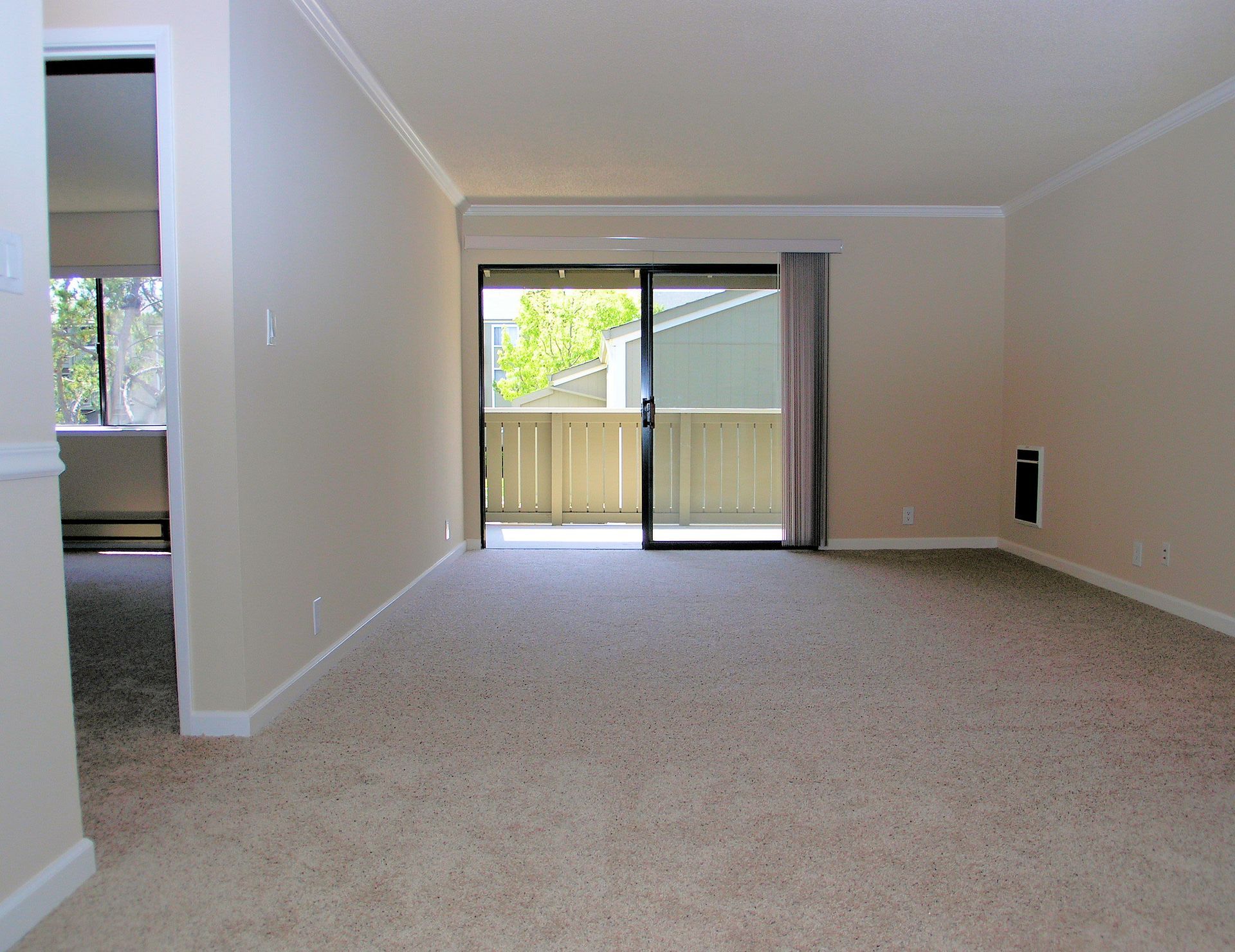 Empty apartment living room with beige walls, carpet, and a sliding balcony door.