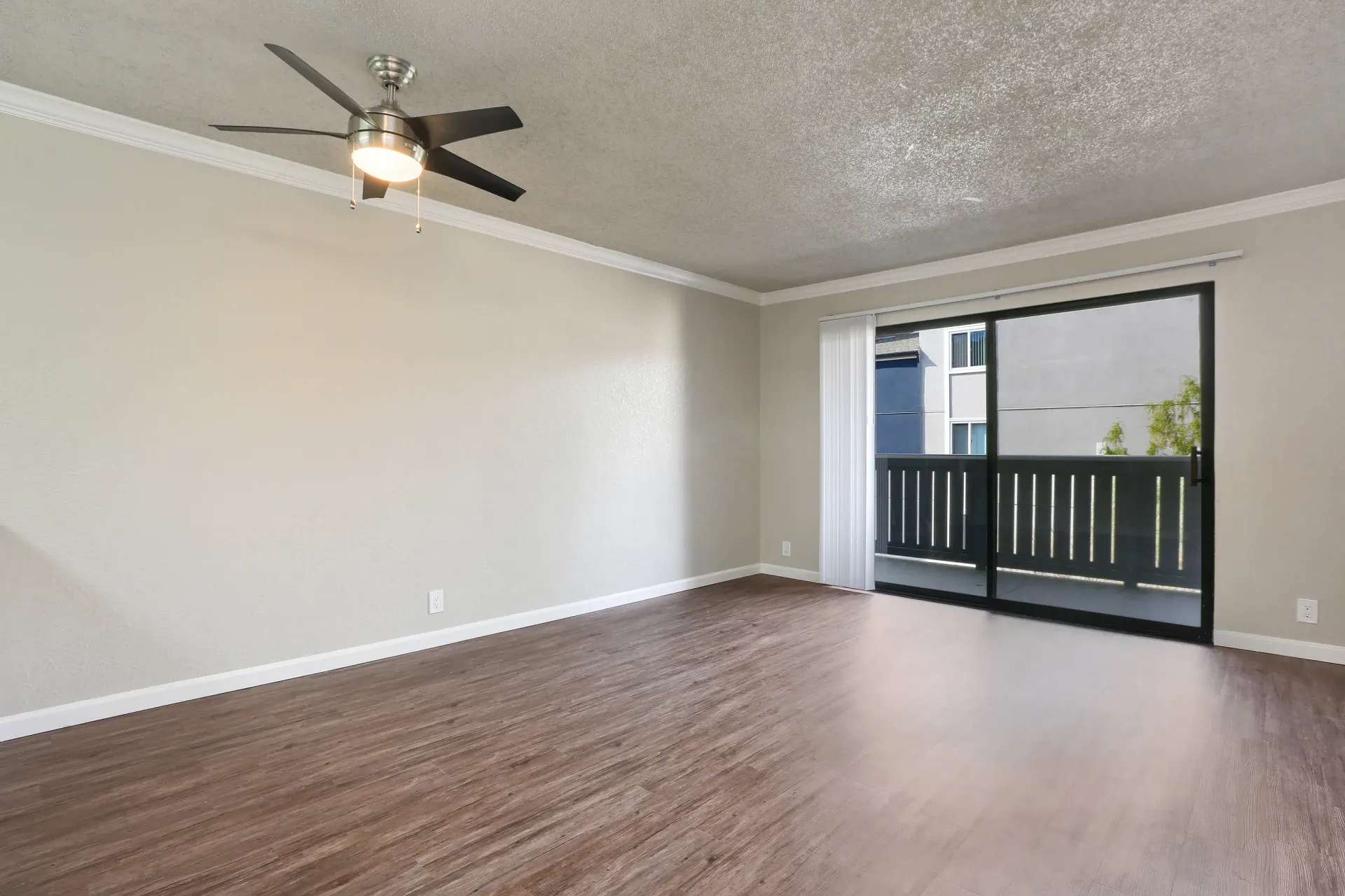 Empty living room in an apartment with sliding glass door to balcony and ceiling fan.
