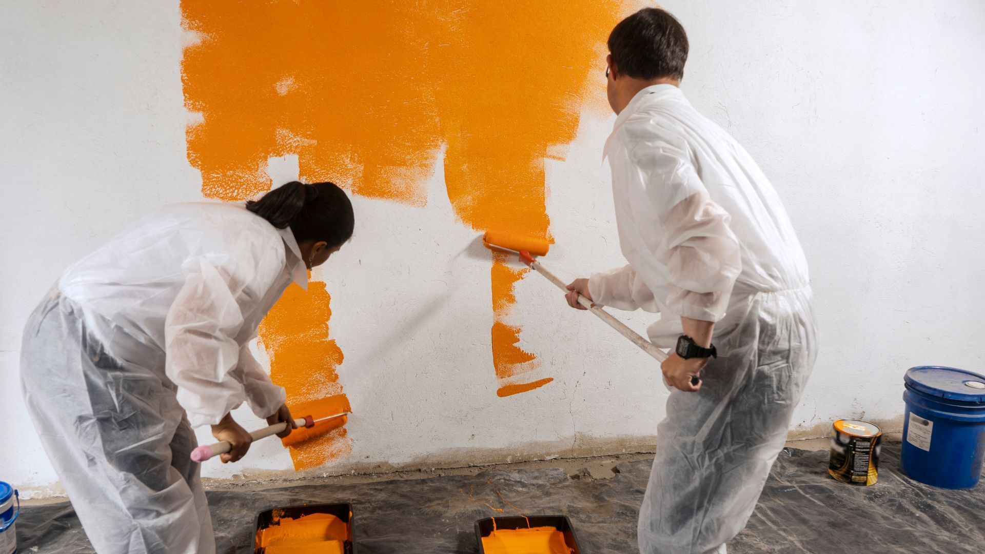 Two people are painting a wall orange.