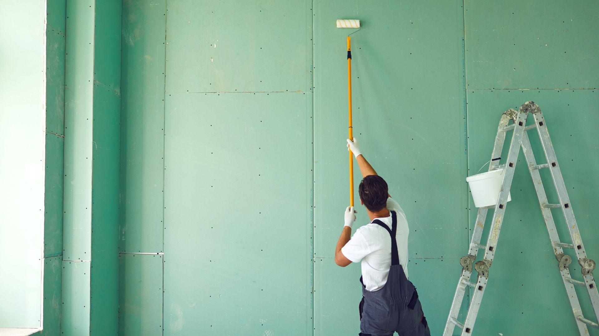 A man is painting a wall with a paint roller.