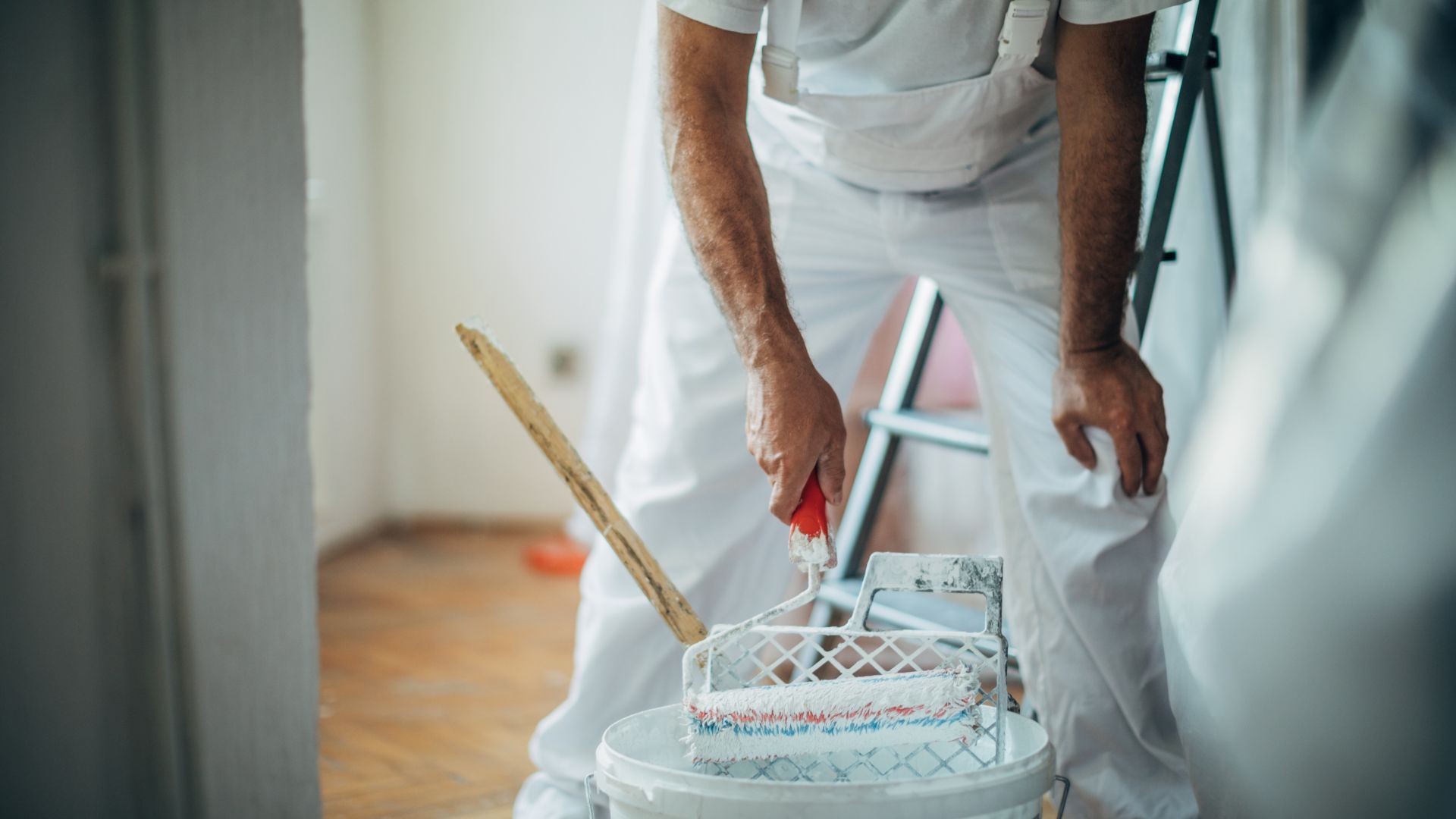 A man is standing next to a bucket of paint and a paint roller.