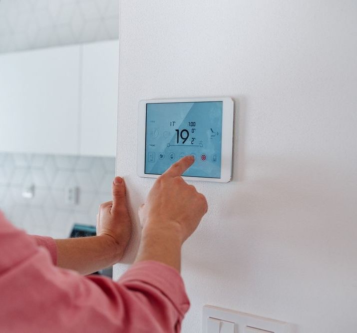 A person is using a tablet to control a thermostat on a wall.