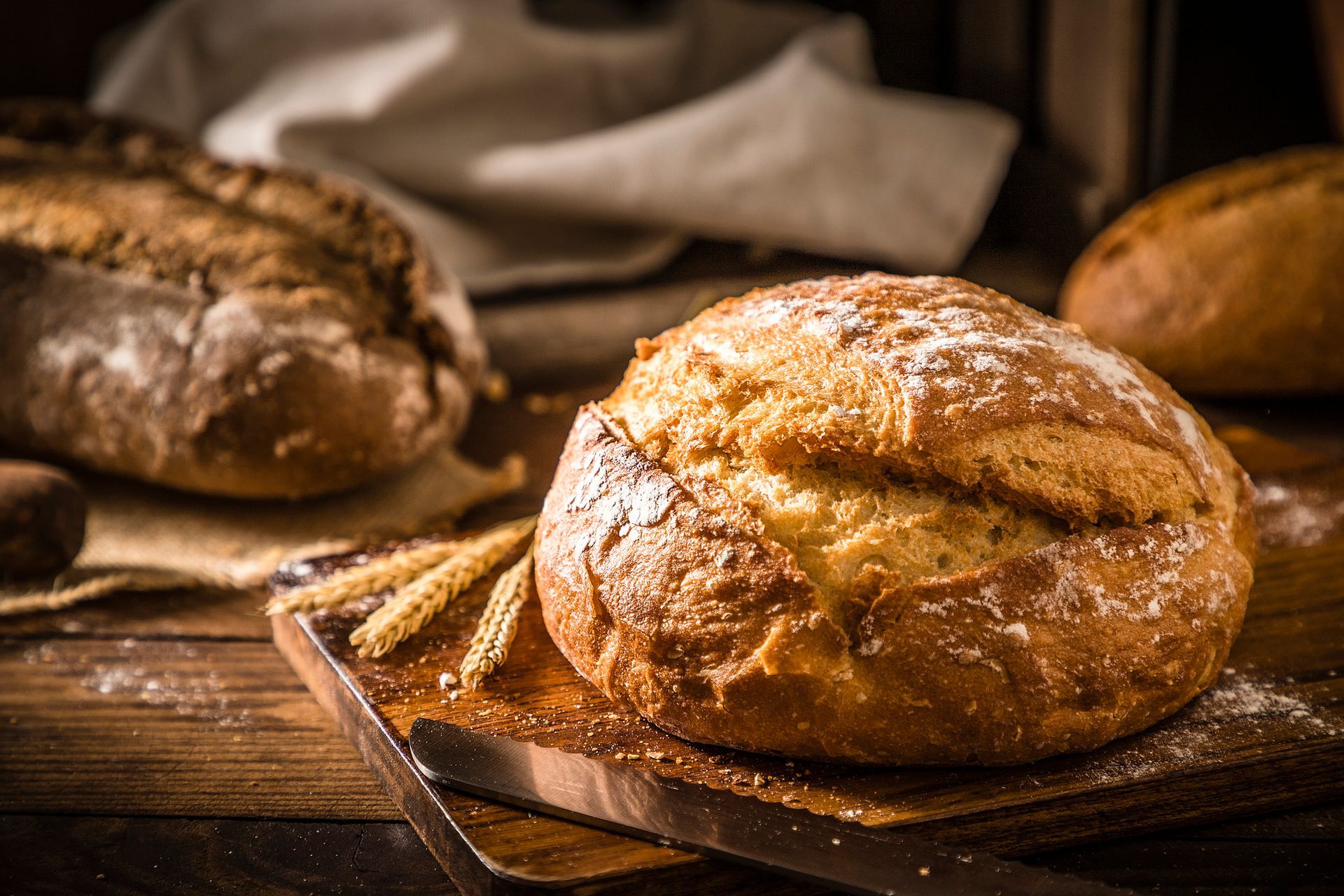 Crusty round loaf of bread on a wooden board with a wheat sprig.