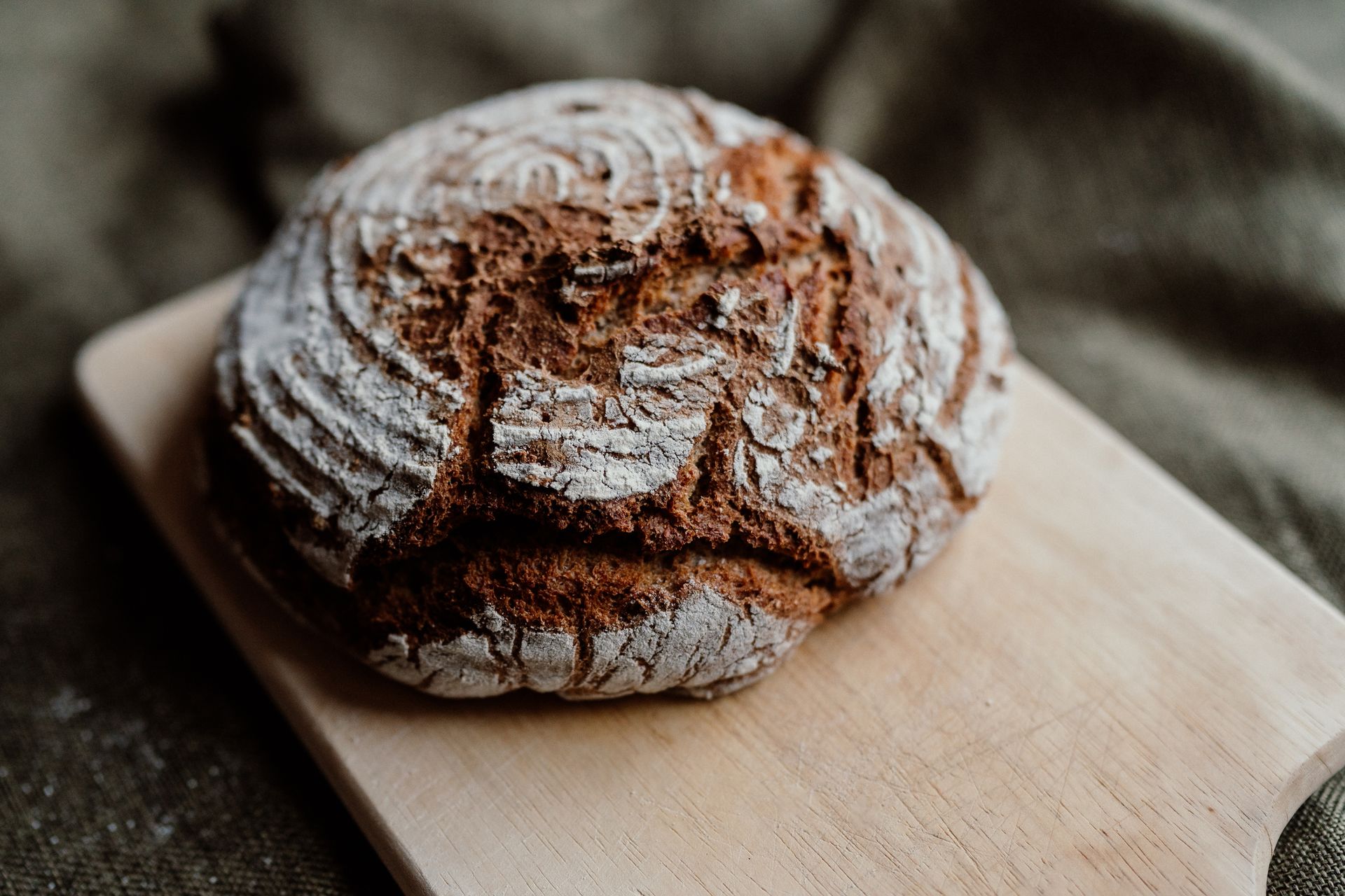 Round loaf of crusty bread on a wooden cutting board.