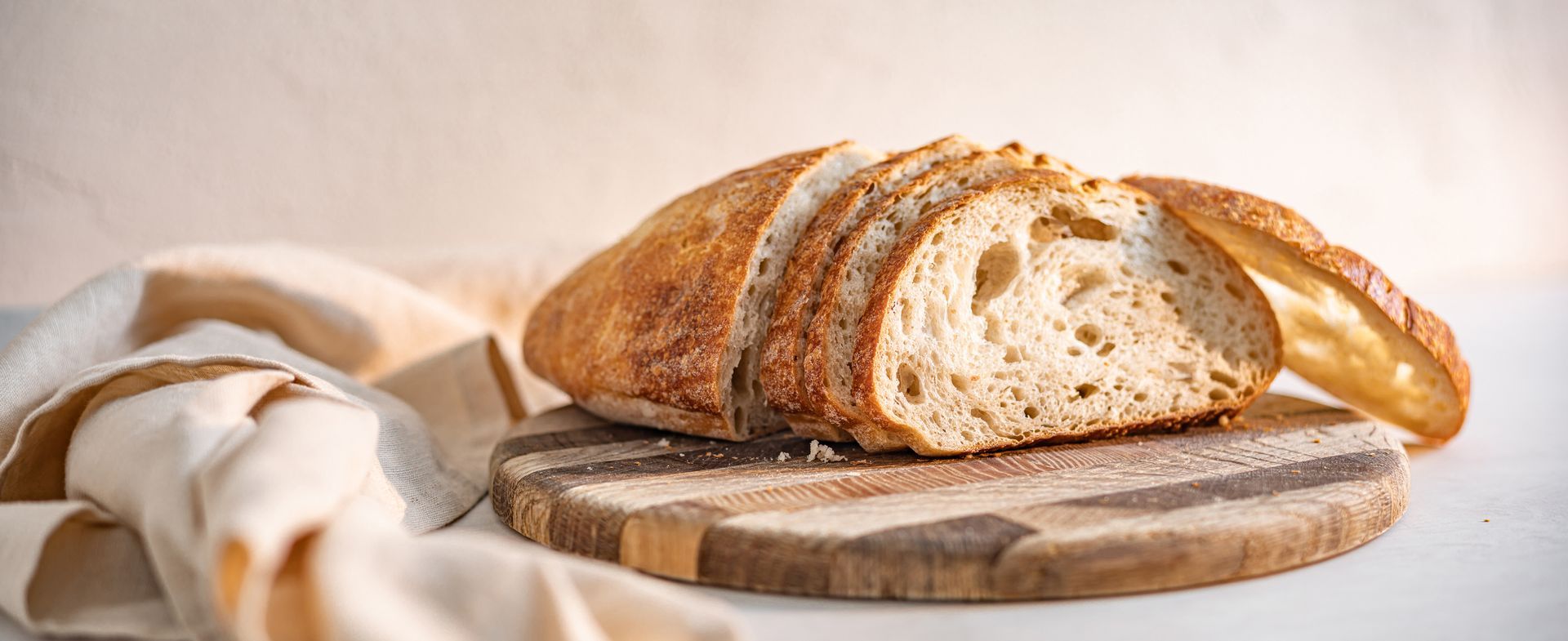 Sliced loaf of bread on a wooden cutting board with a cloth napkin, on a light background.