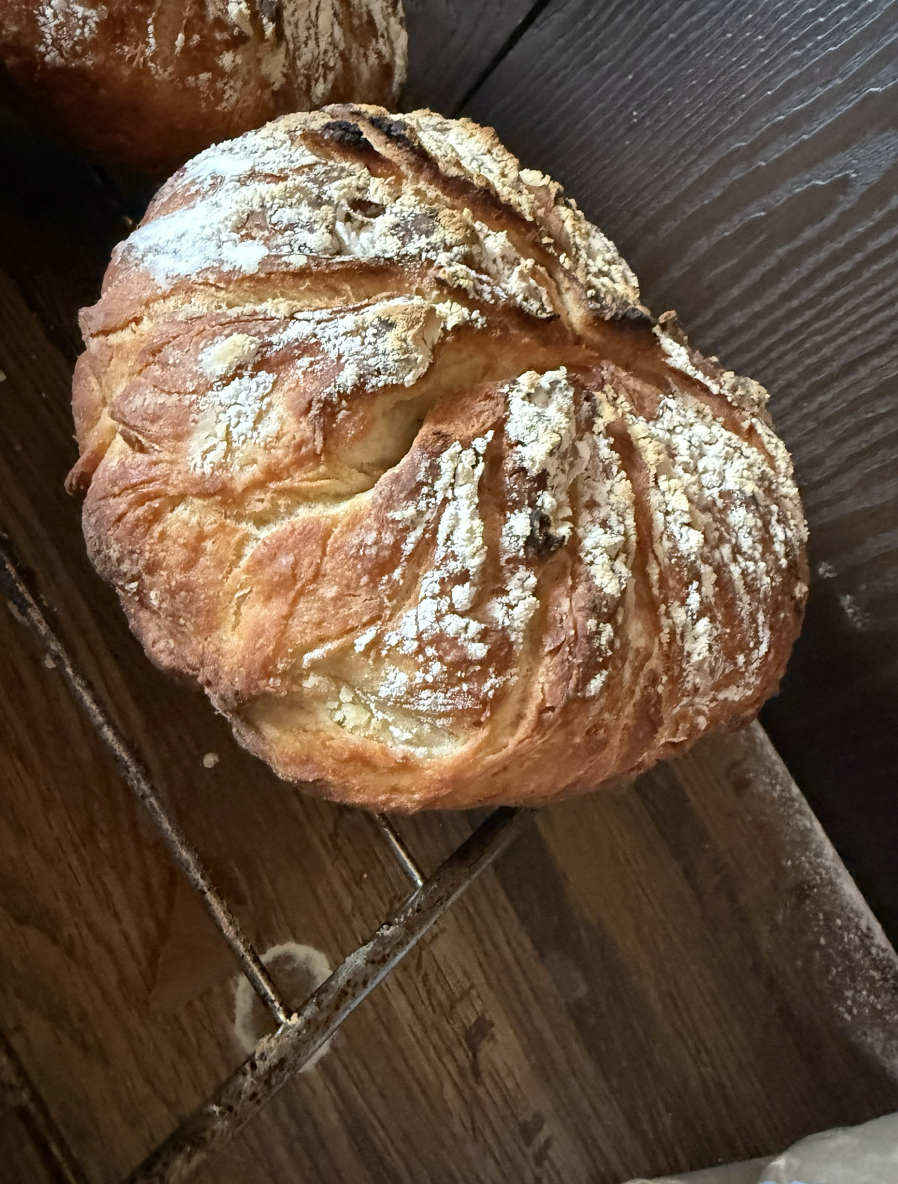 Round loaf of bread, crusty and dusted with flour, resting on a wooden surface.