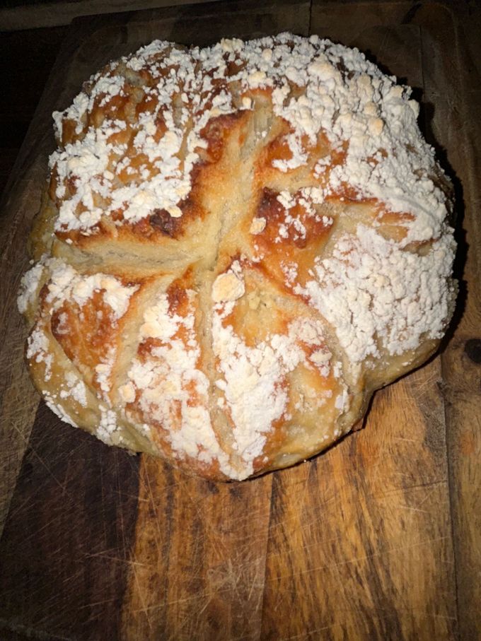 Crusty loaf of bread with a crumb topping, on a wooden cutting board.