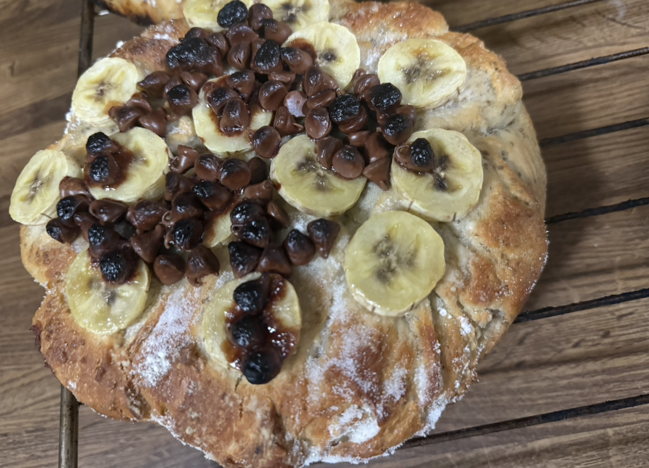 Banana and raisin bread on a wooden surface, with circular banana slices and raisins on top.
