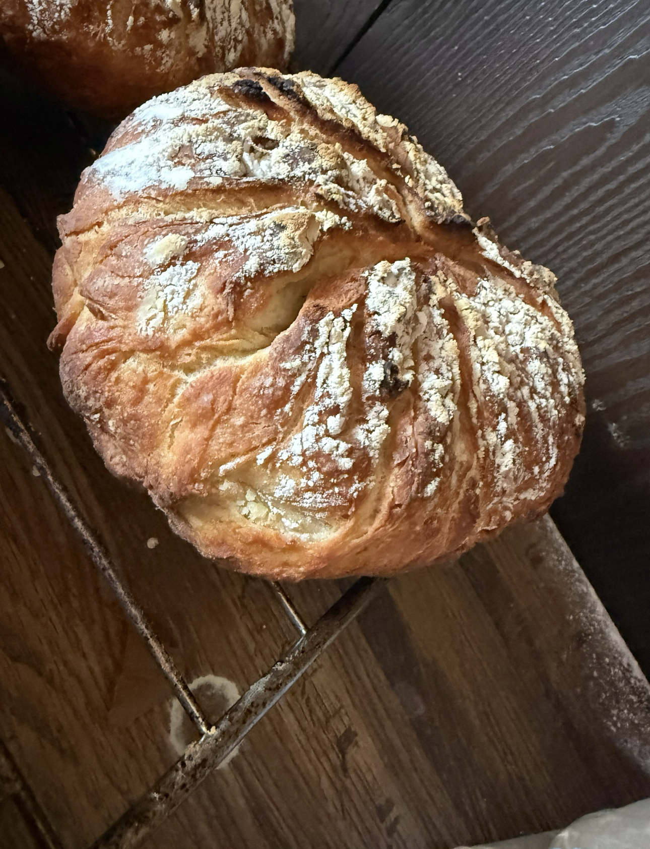 Crusty loaf of bread dusted with flour, resting on a wooden rack.