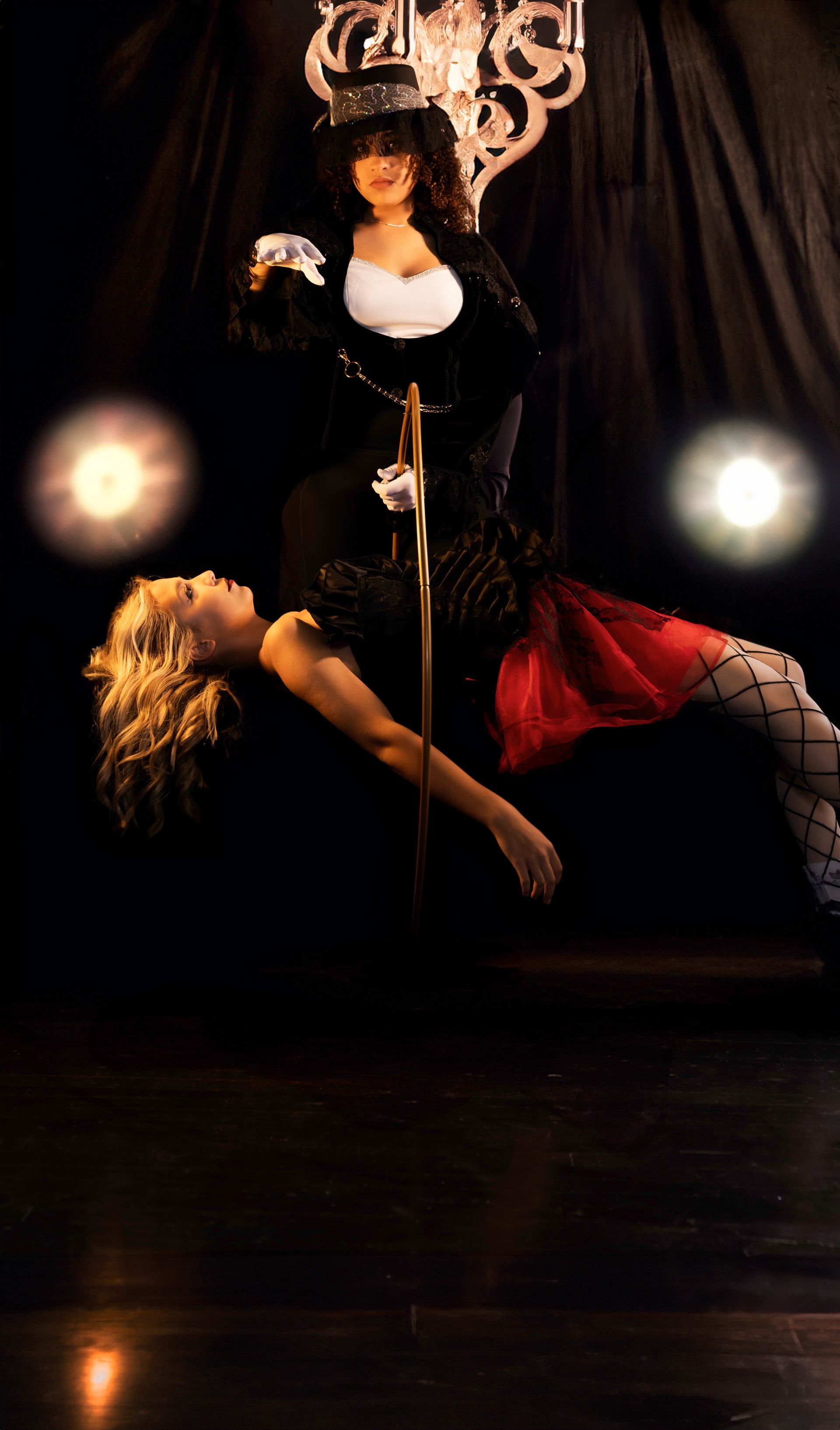 Two women are dancing on a pole in front of a chandelier.