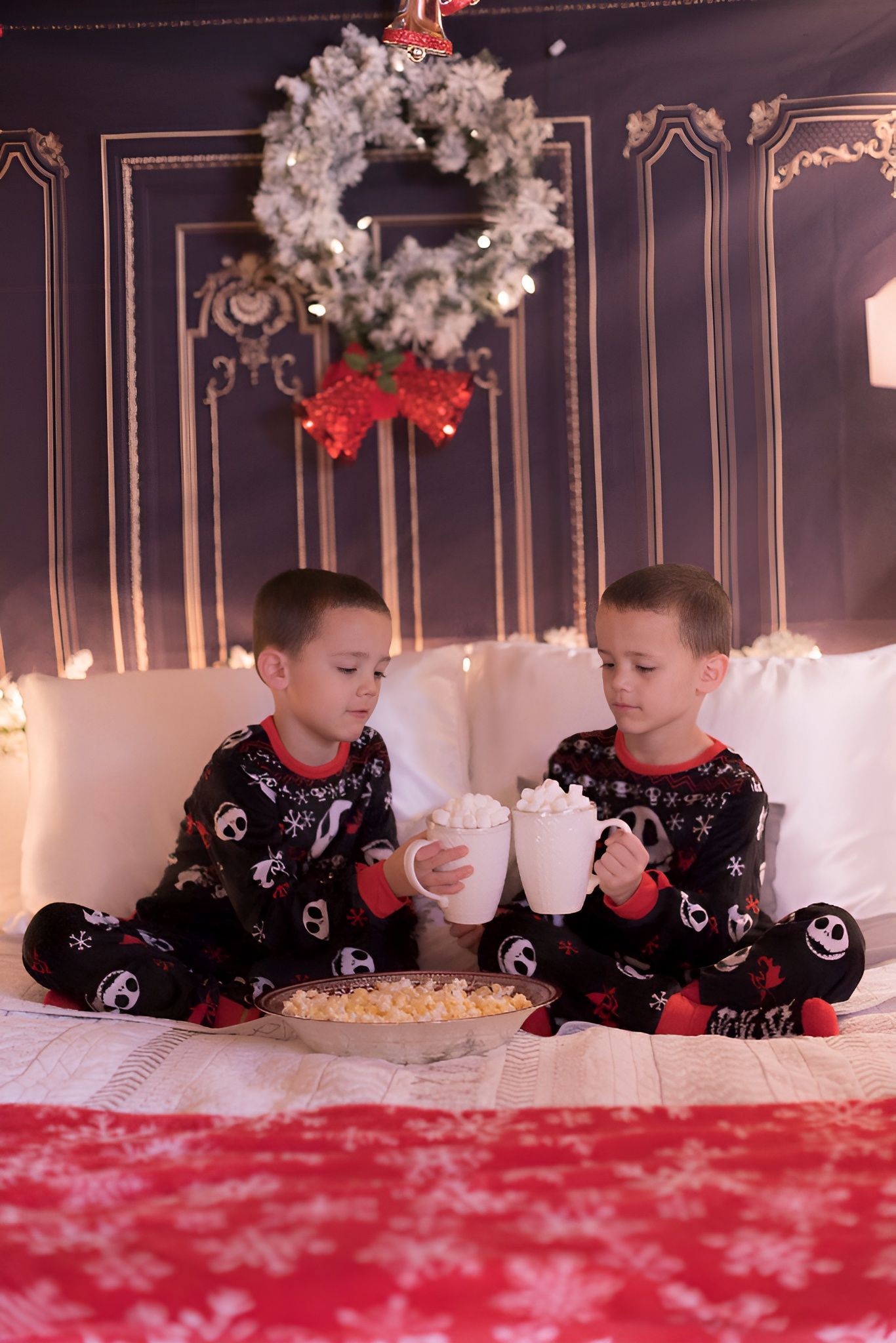 Two young boys are sitting on a bed drinking hot chocolate.