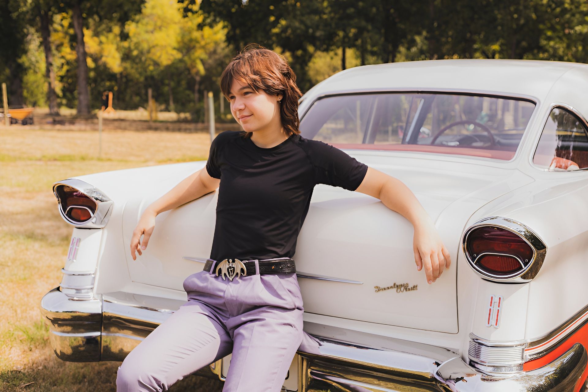 A woman is leaning on the back of a white car.