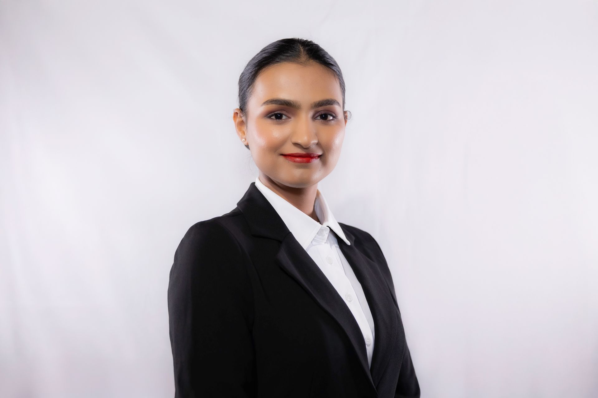 Woman in black blazer and white shirt, smiling, standing in front of a white backdrop.