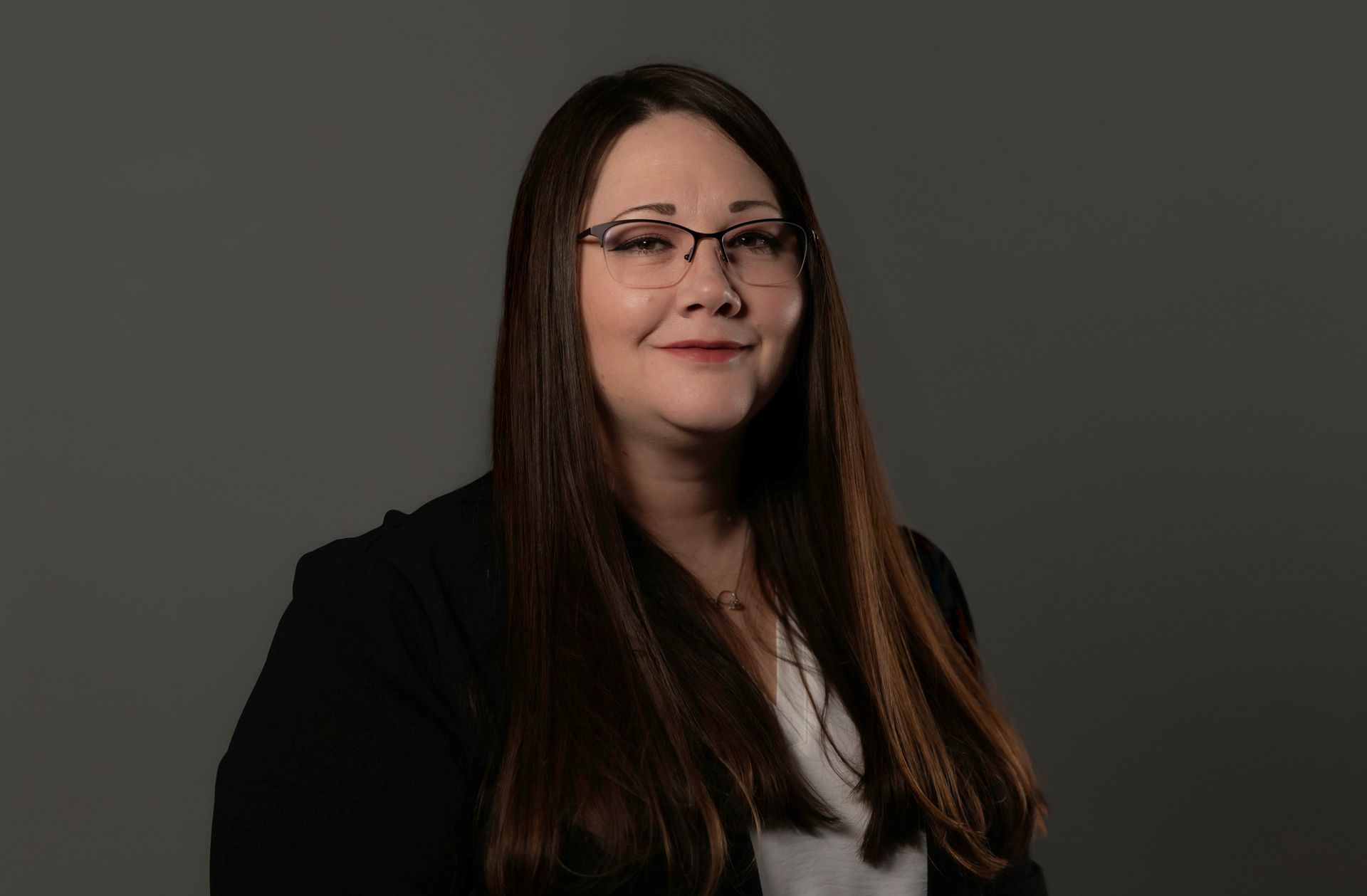 A woman wearing glasses and a black jacket is smiling for the camera.