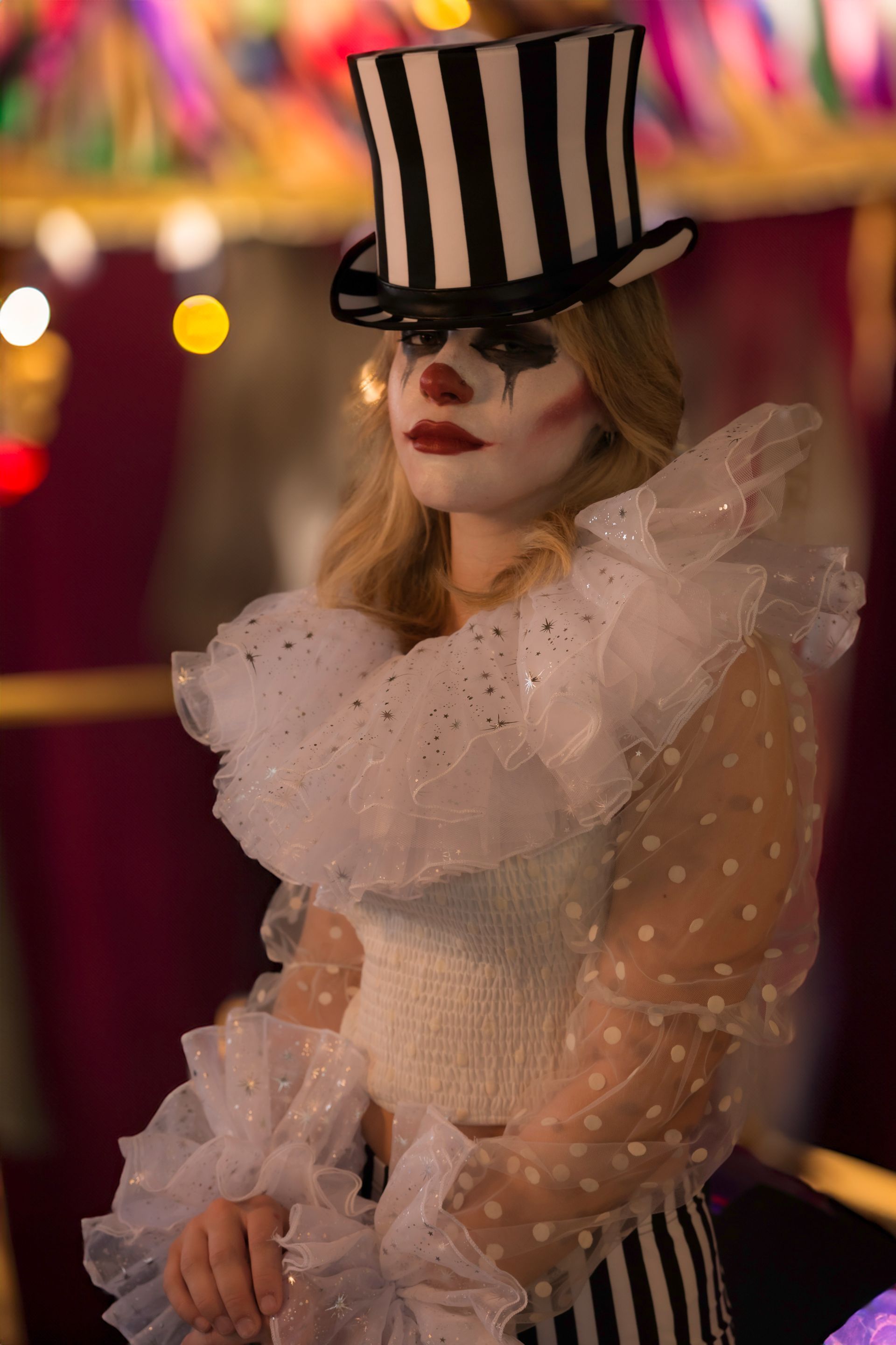 A woman dressed as a clown is wearing a top hat.