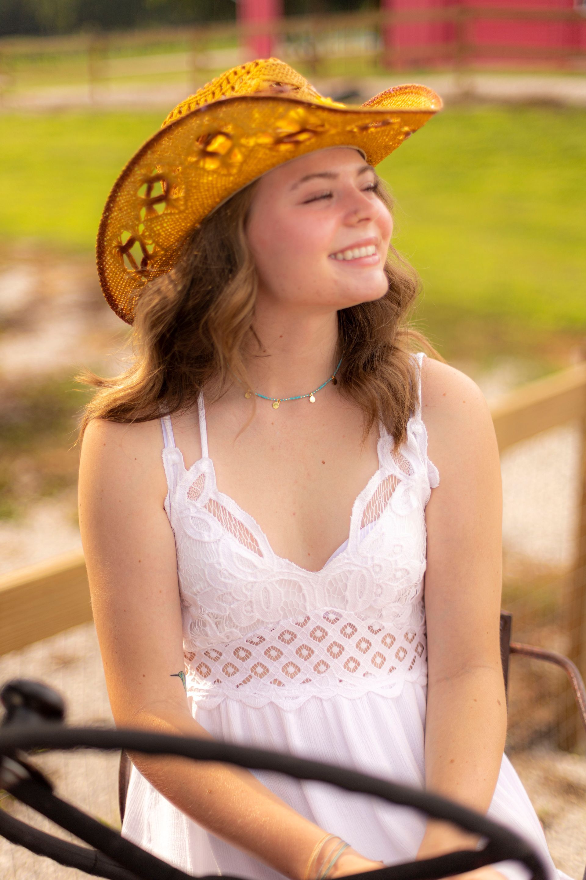 A woman wearing a cowboy hat and a white dress is sitting on a tractor.