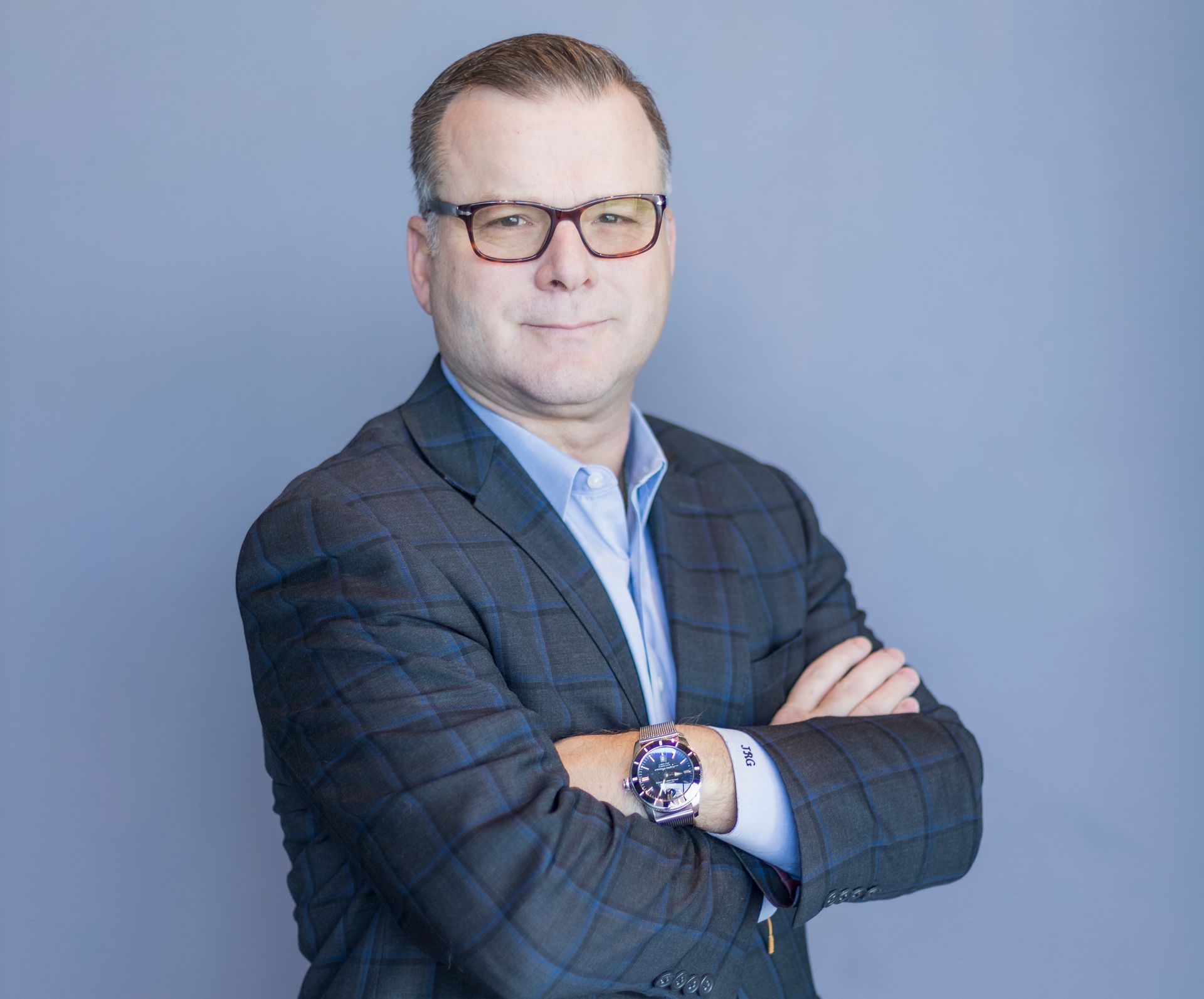 A man in a suit and glasses is standing with his arms crossed.
