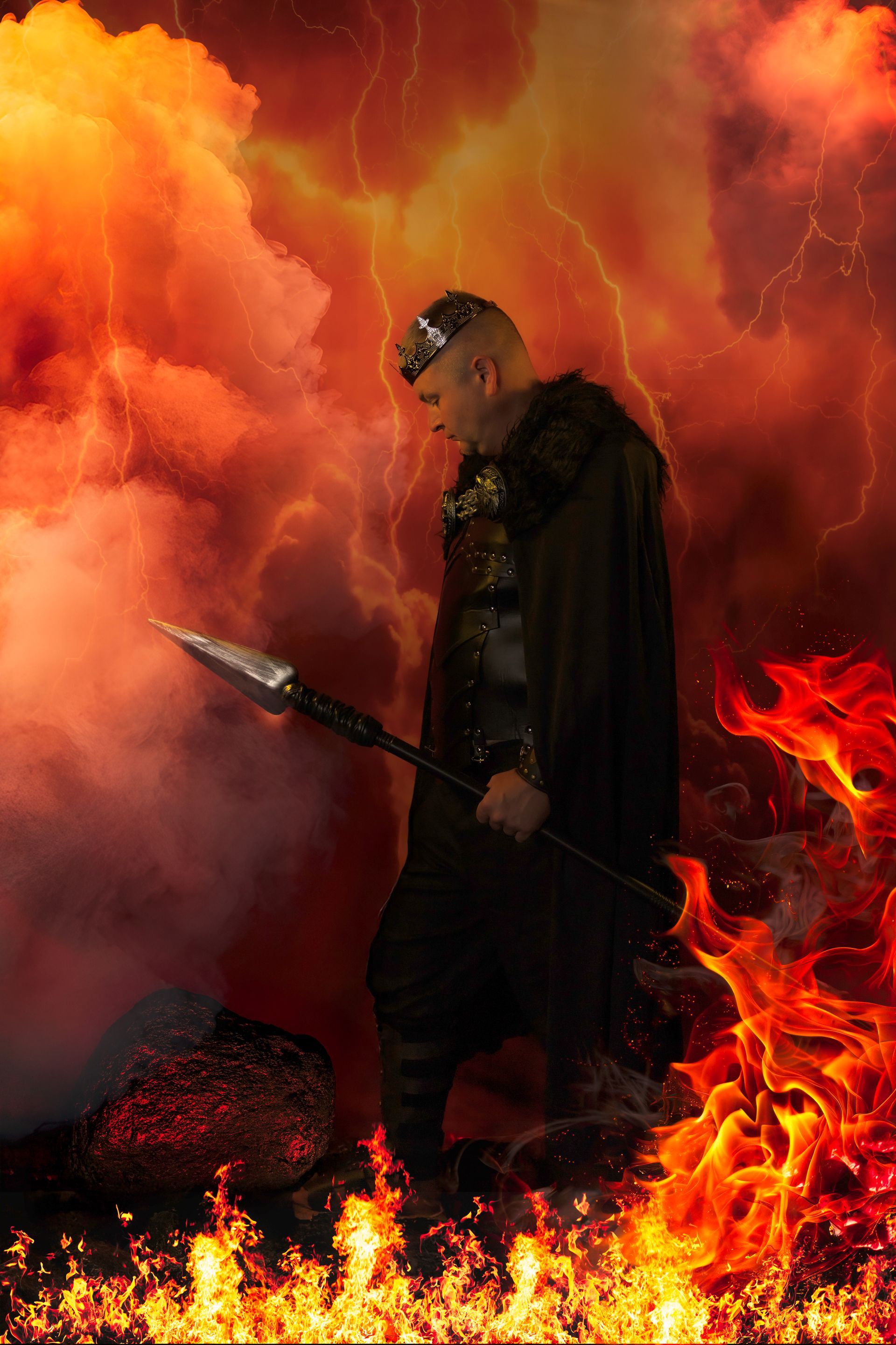 Man in black armor, holding spear, stands in fiery hellscape.