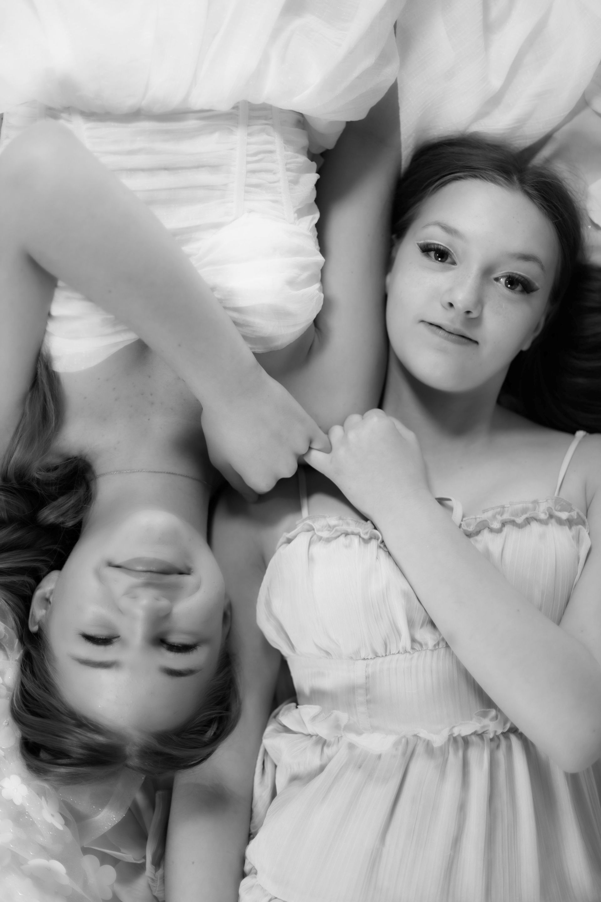 Two girls are laying upside down on a bed.