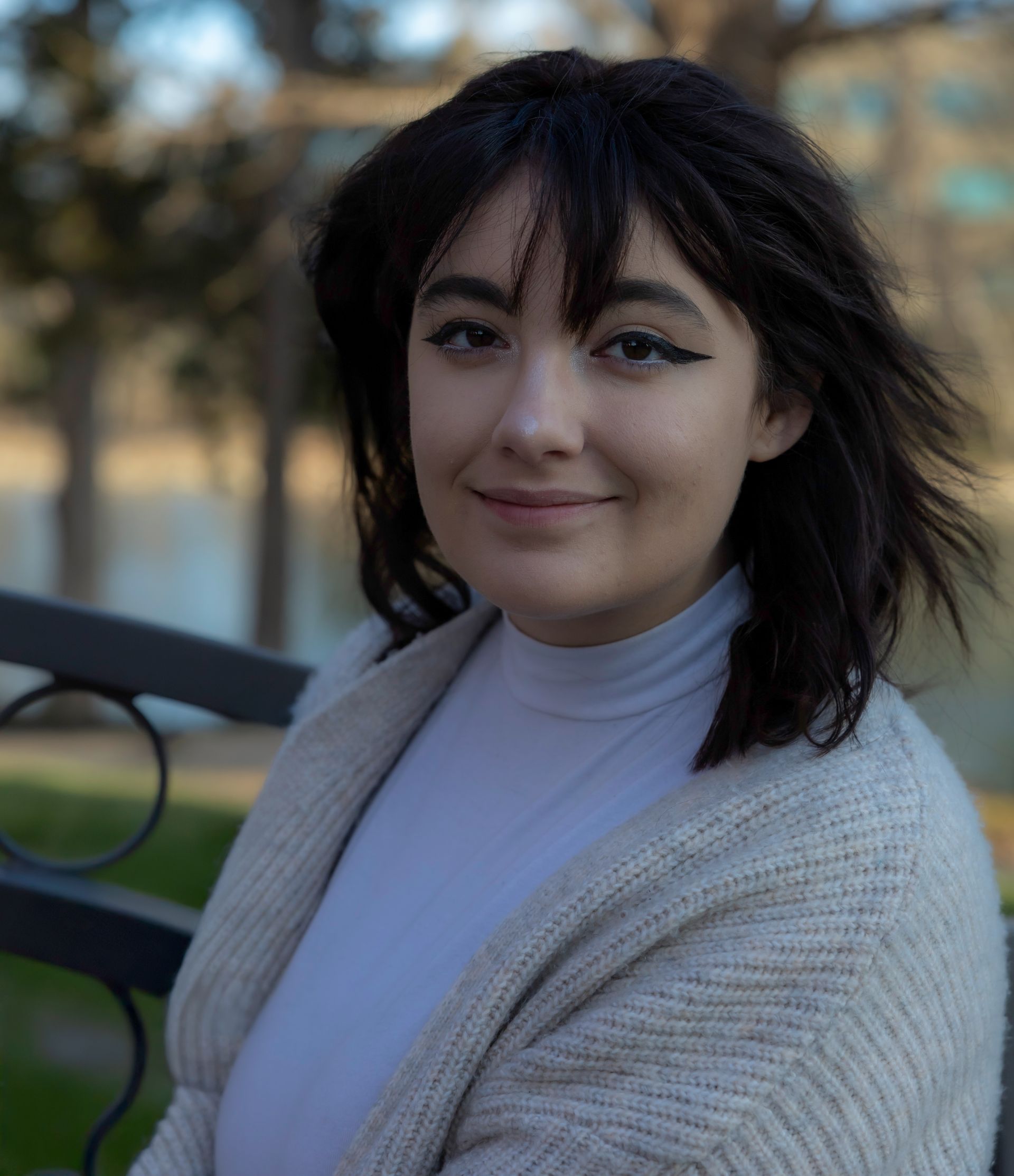 A woman in a white sweater is sitting on a bench and smiling for the camera.