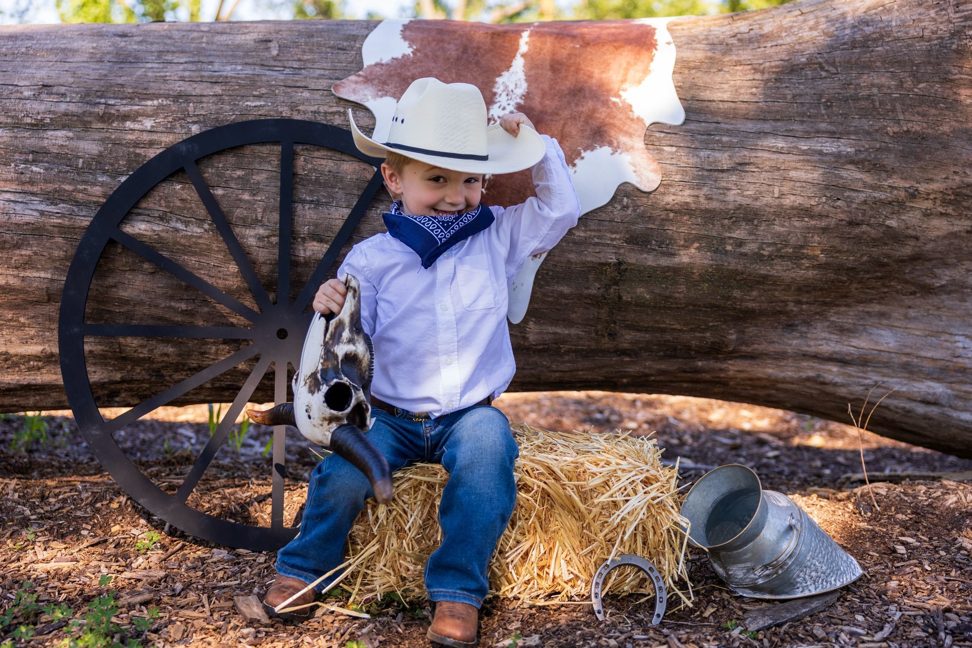 A young boy dressed as a cowboy is sitting on a bale of hay.